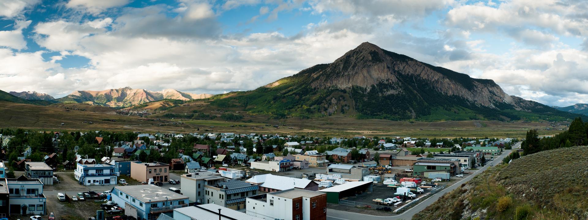 A town nestled in a valley with a large mountain under a cloudy sky.