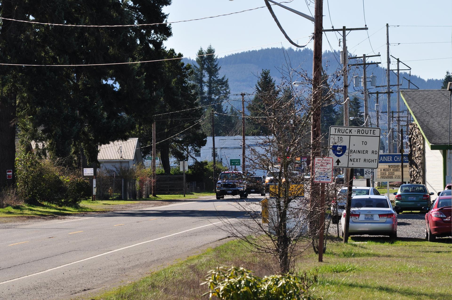 Daylight view of a rural road with cars, utility poles, and distant hills.