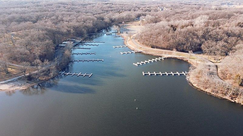 Empty boat docks extend into a calm lake, surrounded by a winter forest.