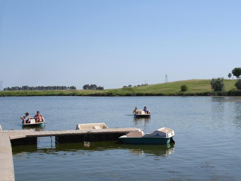 Sunny day on a lake with people in paddle boats near a dock.