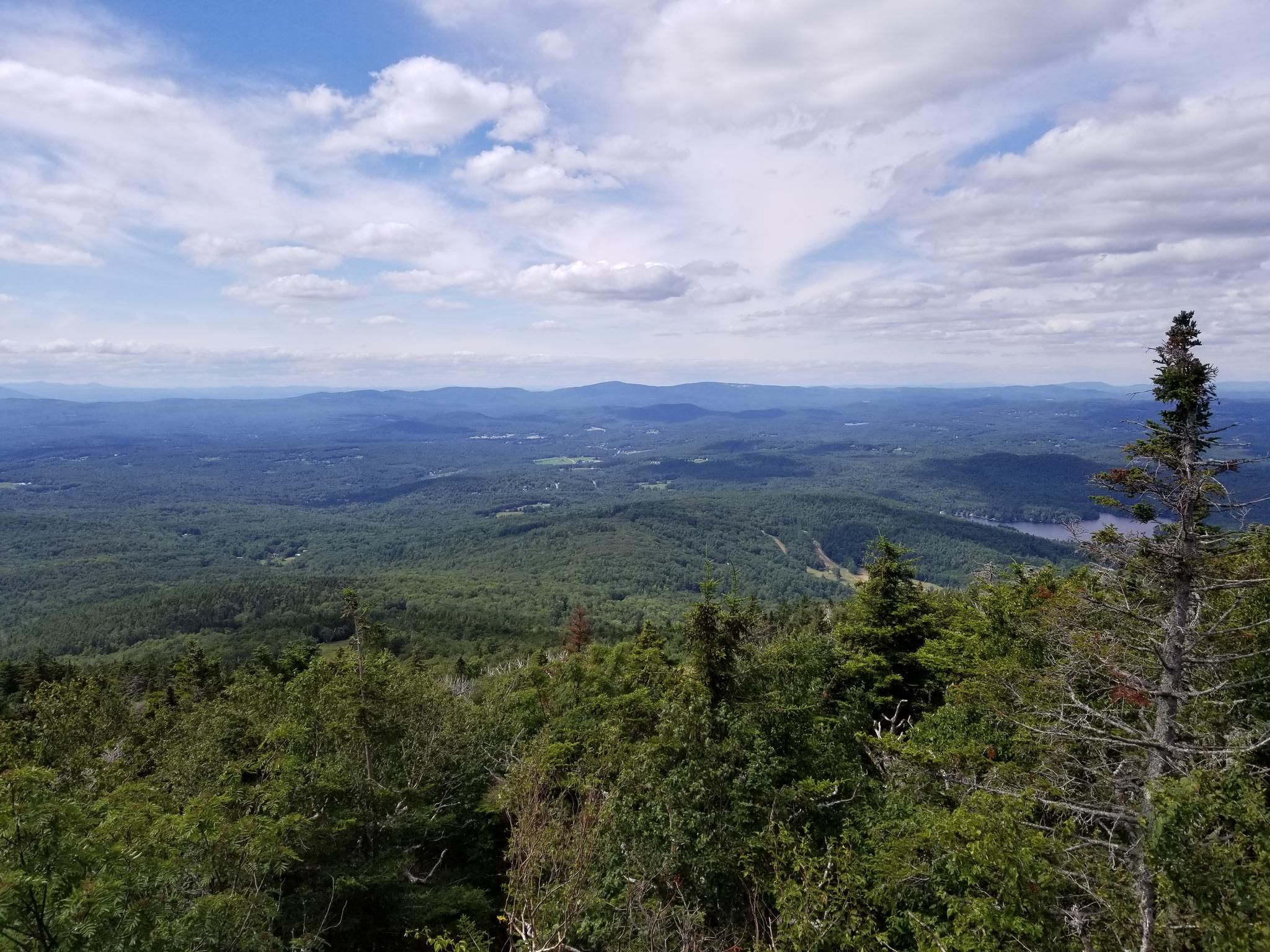 Vast green forest and distant mountains under a cloudy blue sky. - Lake Sunapee Lighthouse – Mount Summit loop from Newbury