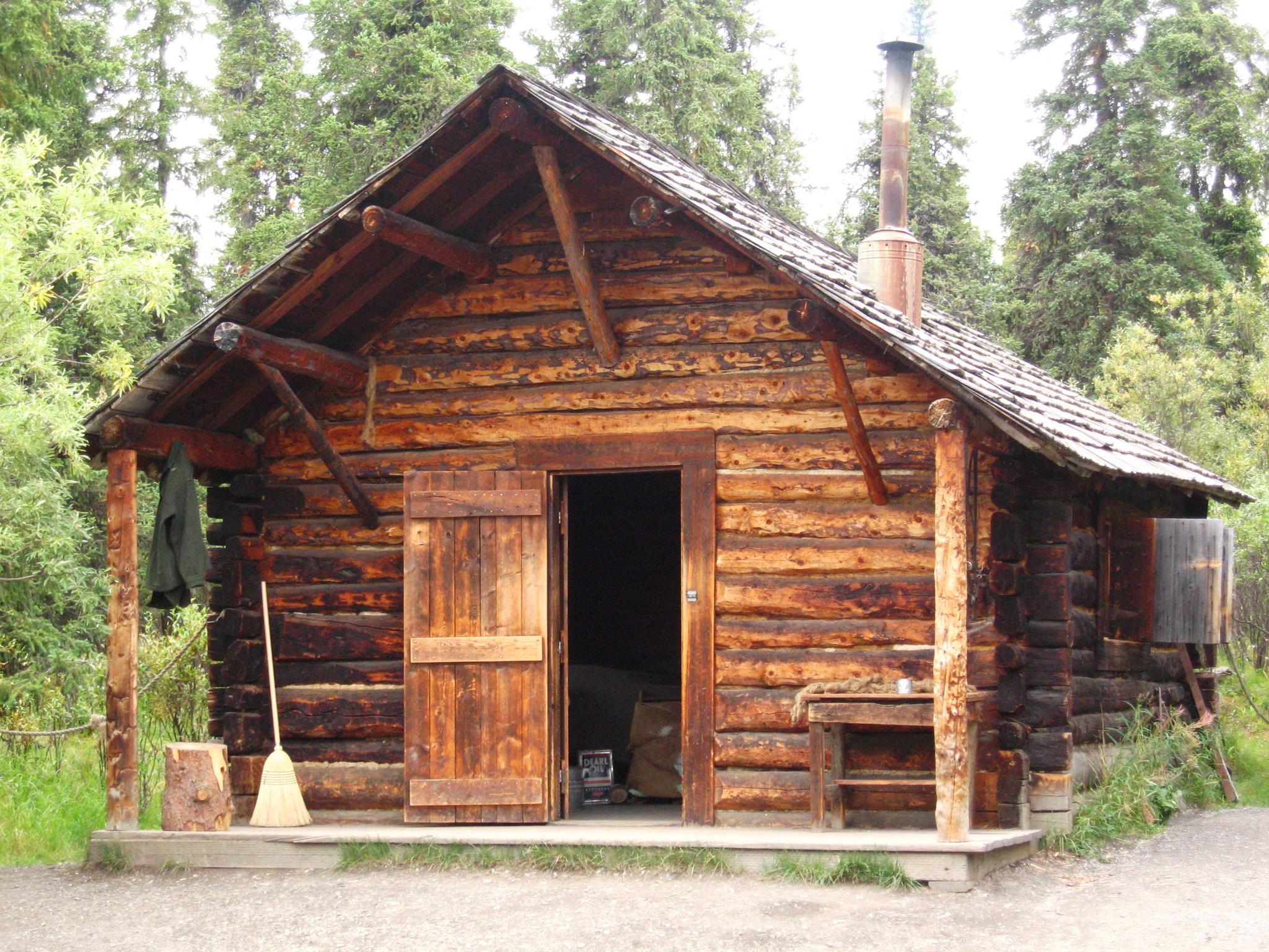 A rustic log cabin with an open door, surrounded by tall trees.