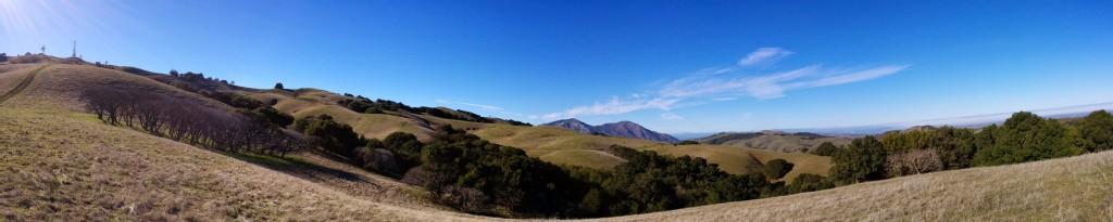 Panoramic view of rolling hills with dry grass and scattered trees under a clear sky.