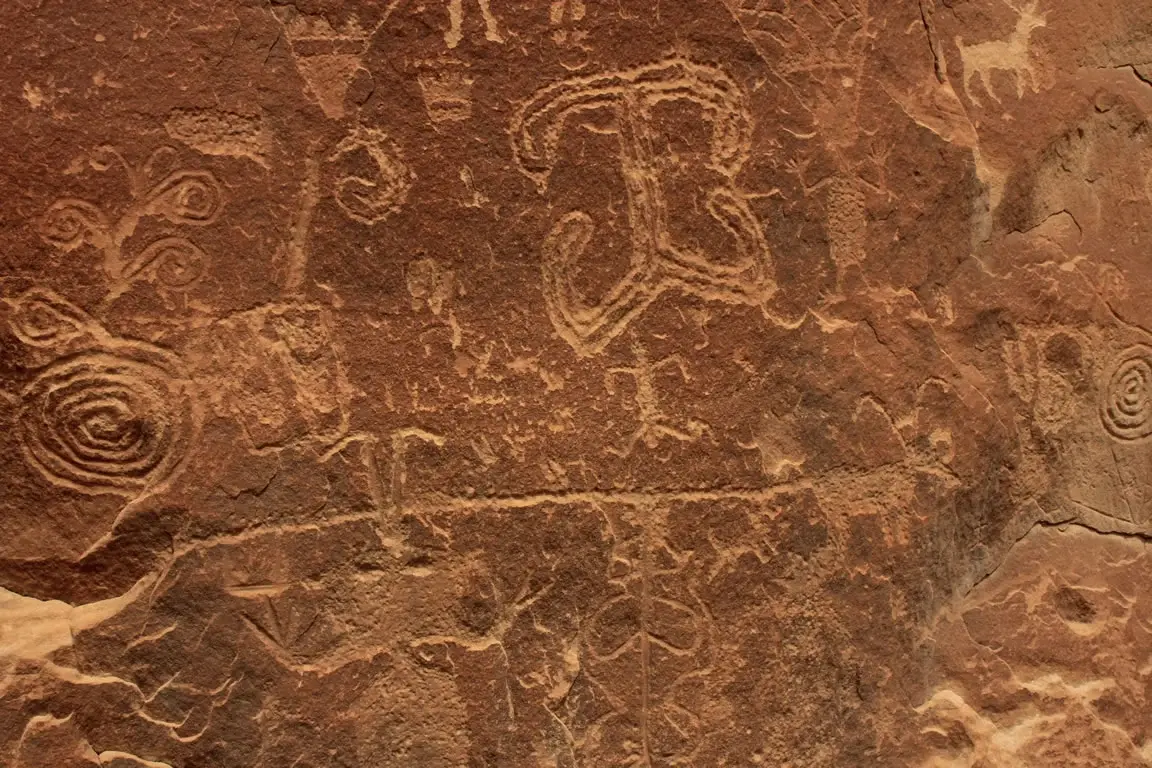 Ancient petroglyphs carved into a reddish-brown rock face under natural light.