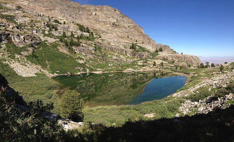 Clear mountain lake reflecting rocky slopes and blue sky on a sunny day.