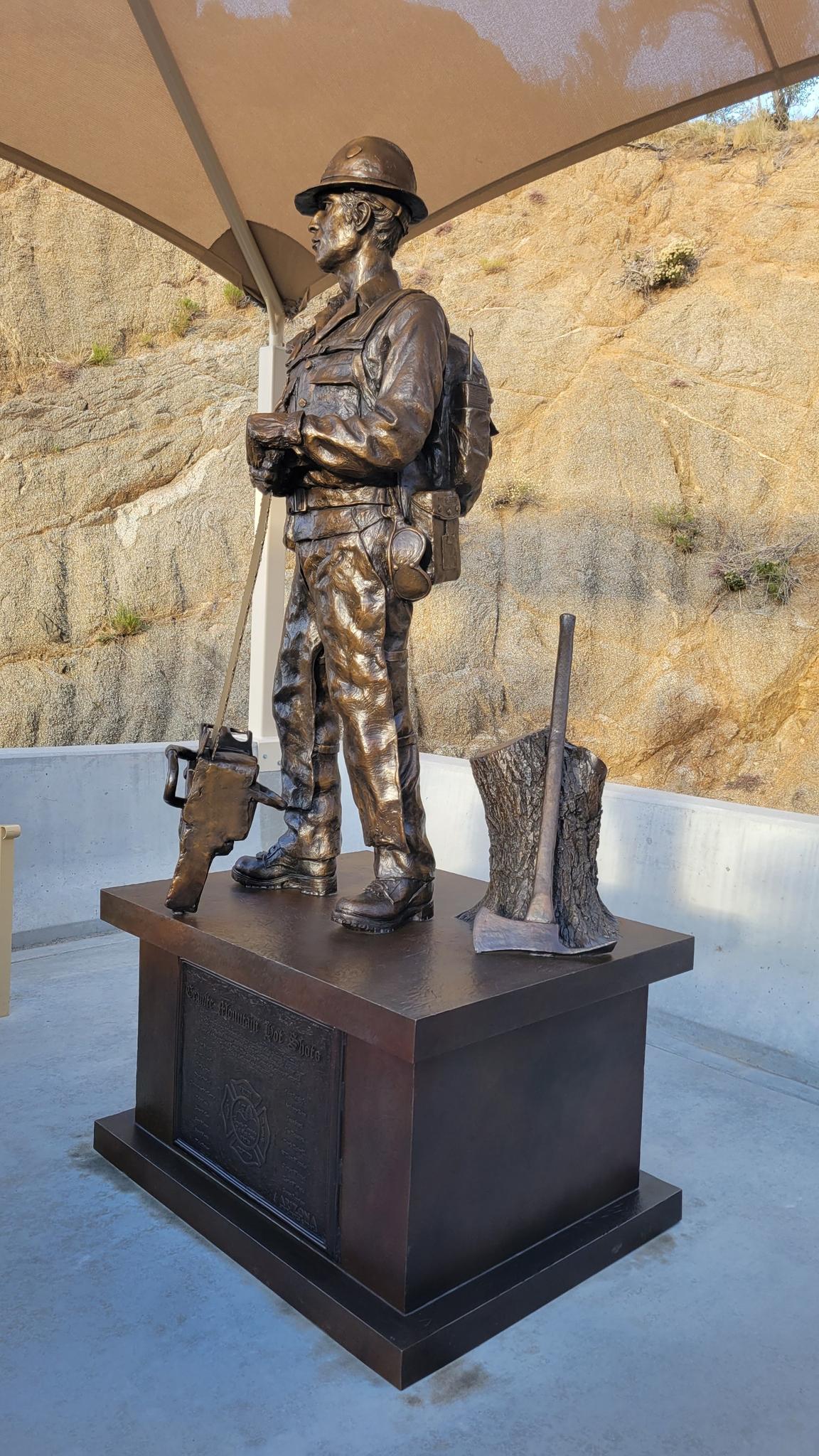Bronze statue of a person in uniform with tools, under a canopy.