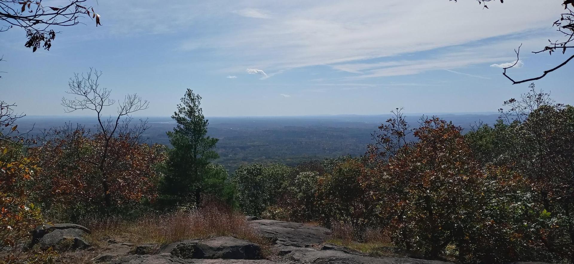 Panoramic view from a rocky mountain overlook with autumn trees under a blue sky.