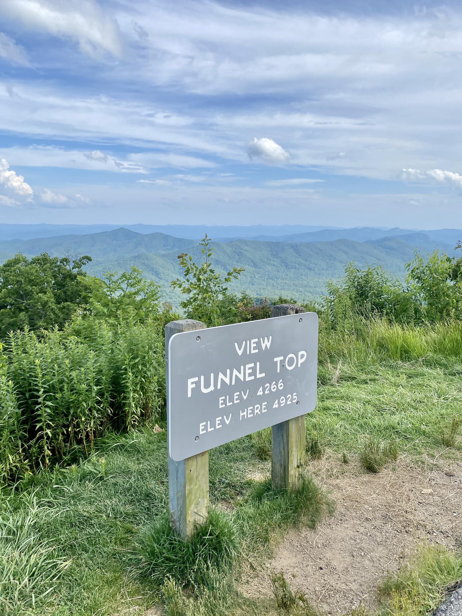 A wooden sign in a grassy area overlooks a distant mountain range.