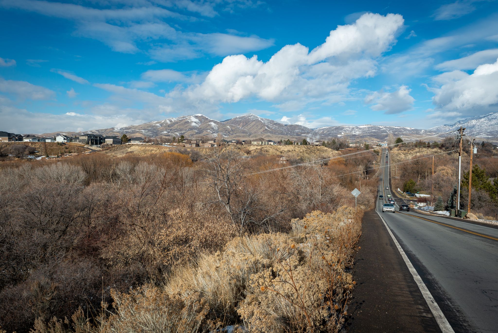 Long road through dry hills, distant snowy mountains, and cars under a cloudy sky. - Dry Creek Reservoir – Draper Utah Temple loop from Draper Utah Temple