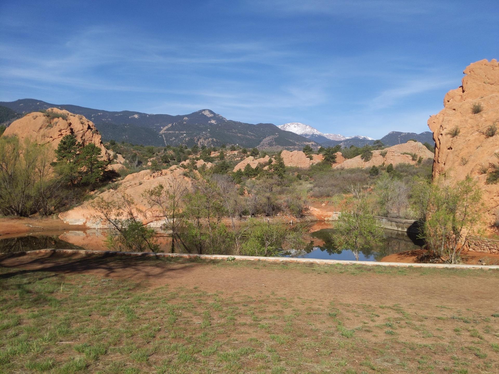 Sunny view of a pond reflecting mountains and red rock formations under blue sky.