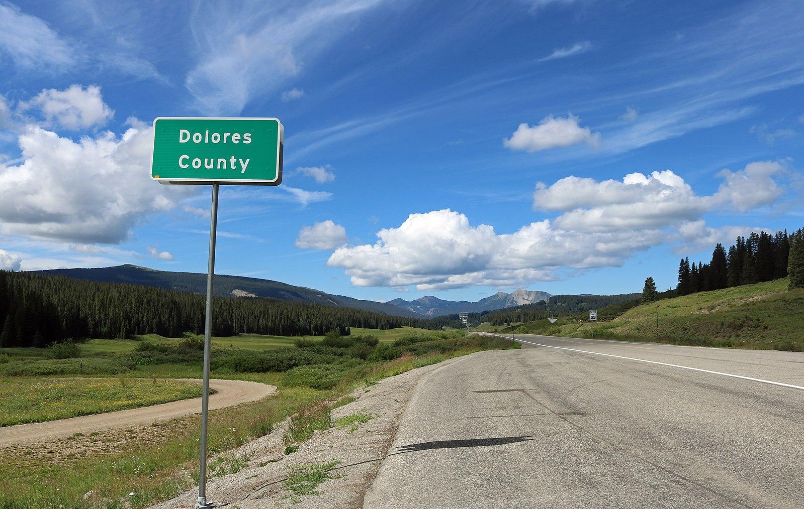 A highway sign stands beside a road winding through a mountain landscape.