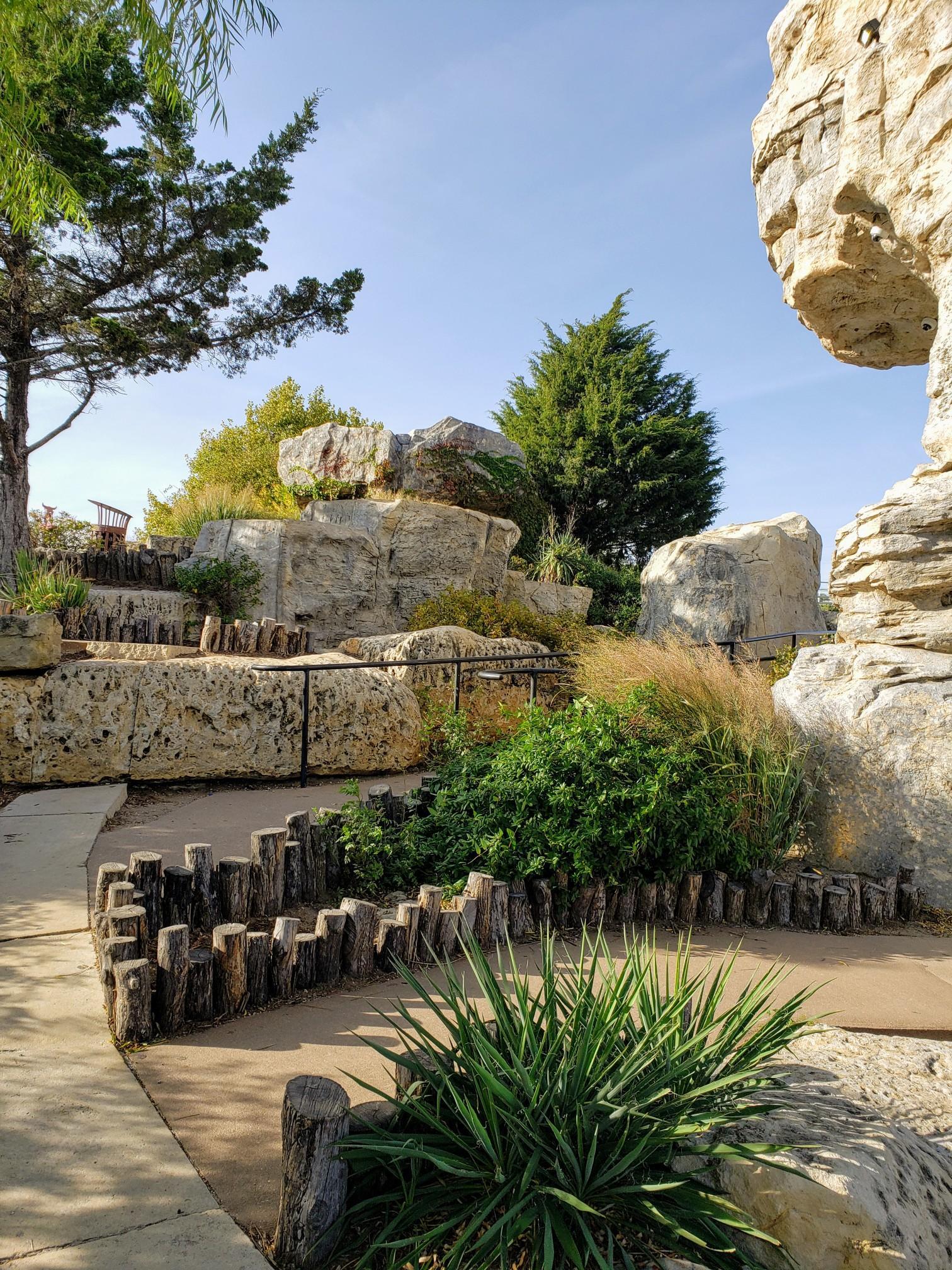 Sunny view of a winding path through large rock formations and green plants.