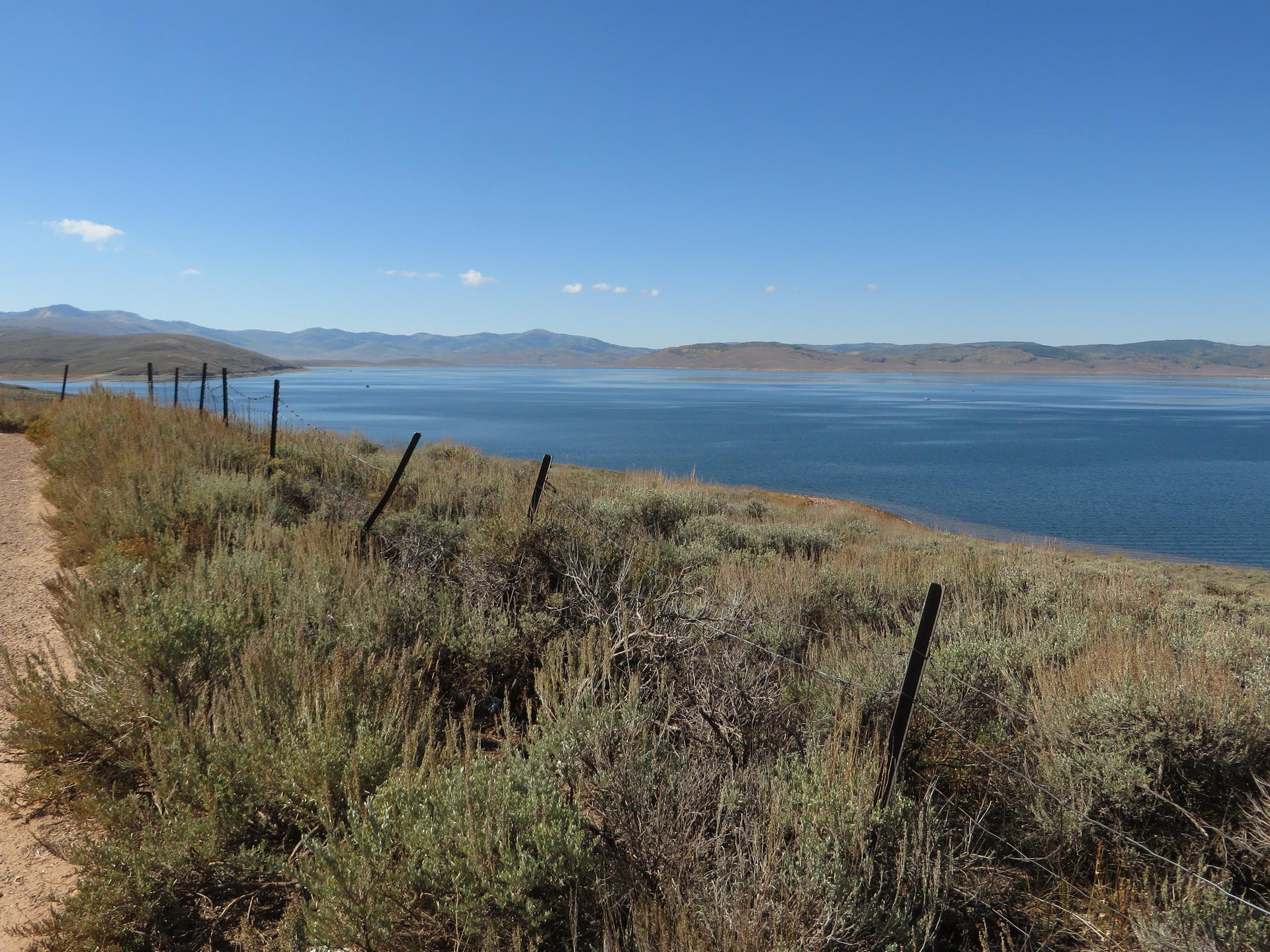 Vast blue lake with distant mountains under a clear sky, dry foreground.