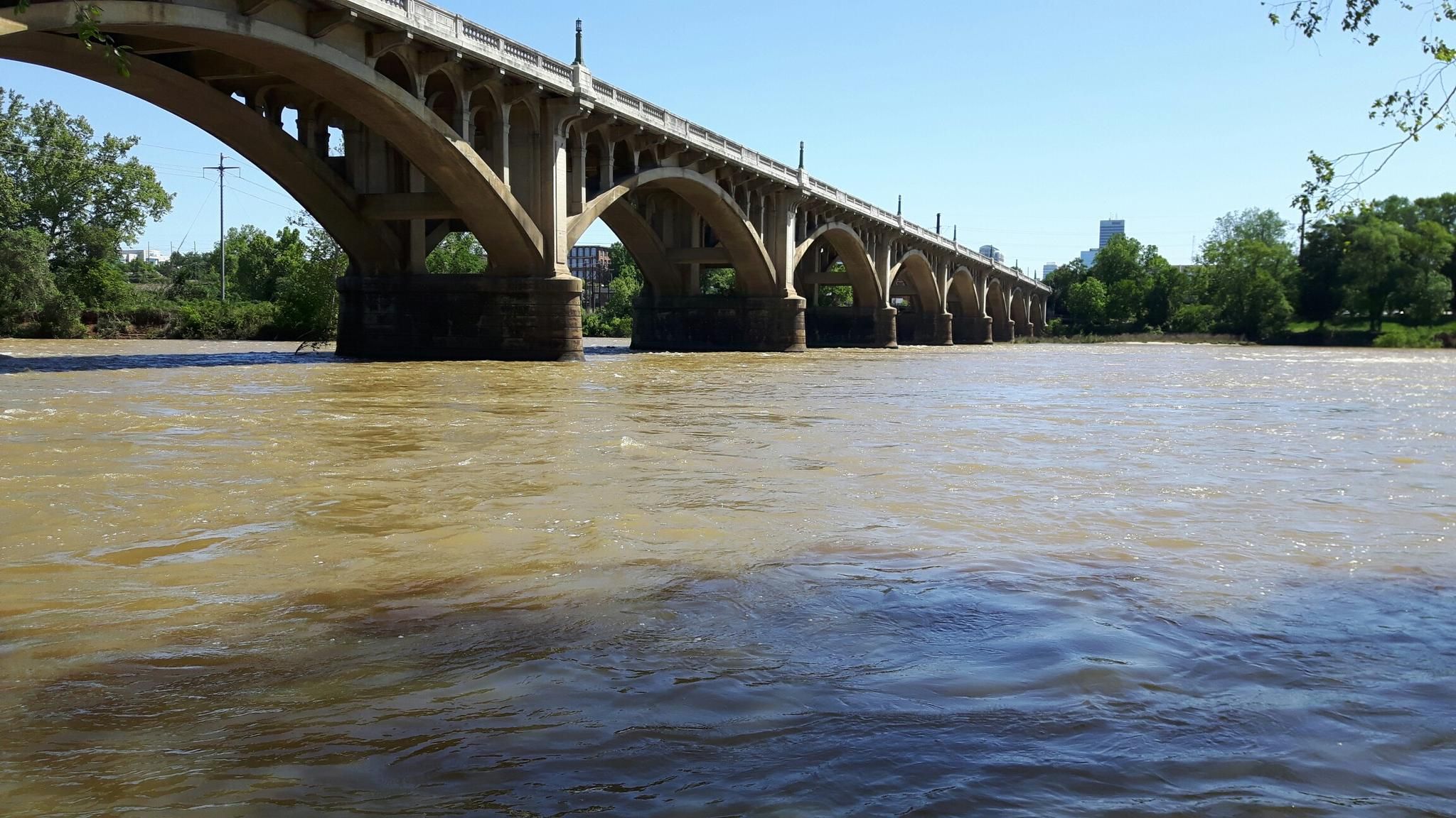 A long arched bridge spans a wide river under a clear, bright sky. - Three Rivers Greenway Loop