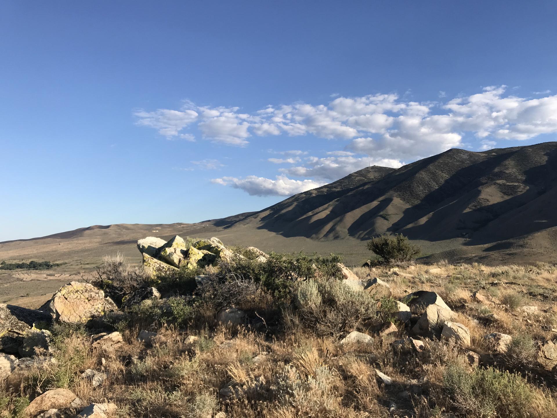 Rocky, arid landscape with distant mountains under a bright, partly cloudy sky.