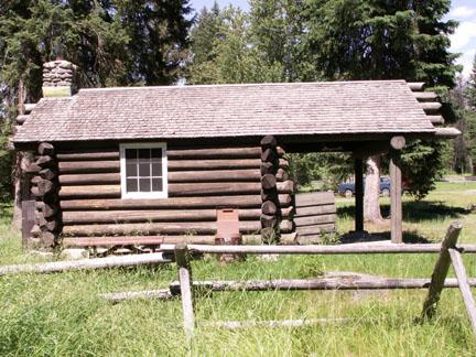 Rustic log cabin with a wooden fence in a sunny, grassy clearing.