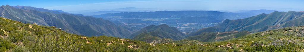 Panoramic view of vast, green, rugged mountains and valleys under a blue sky.