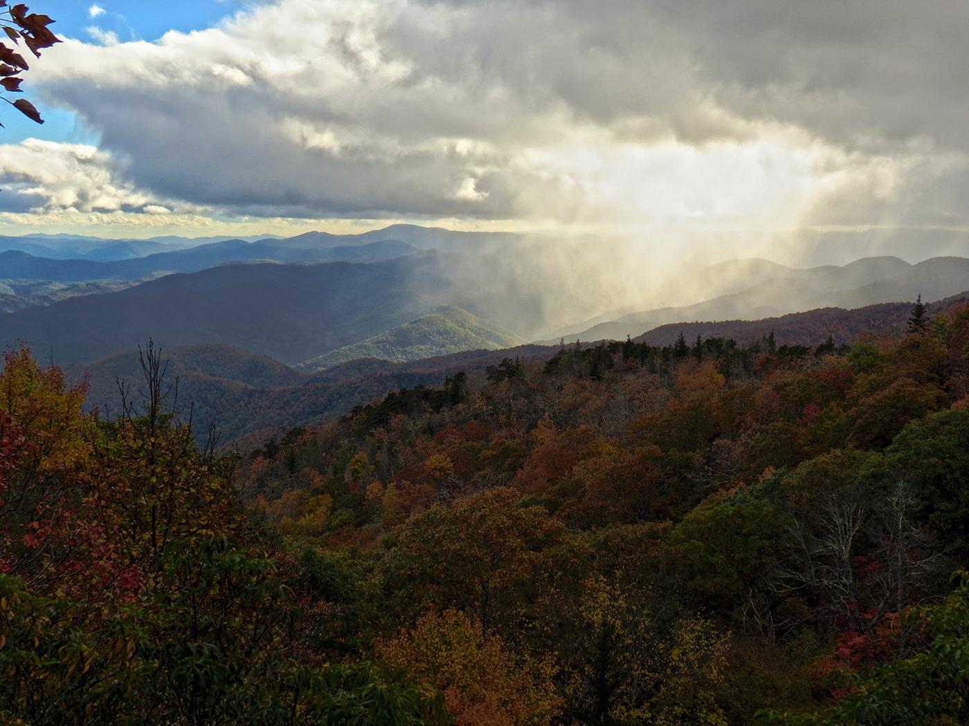 Autumn mountain landscape with rain falling from dramatic clouds, sun breaking through.
