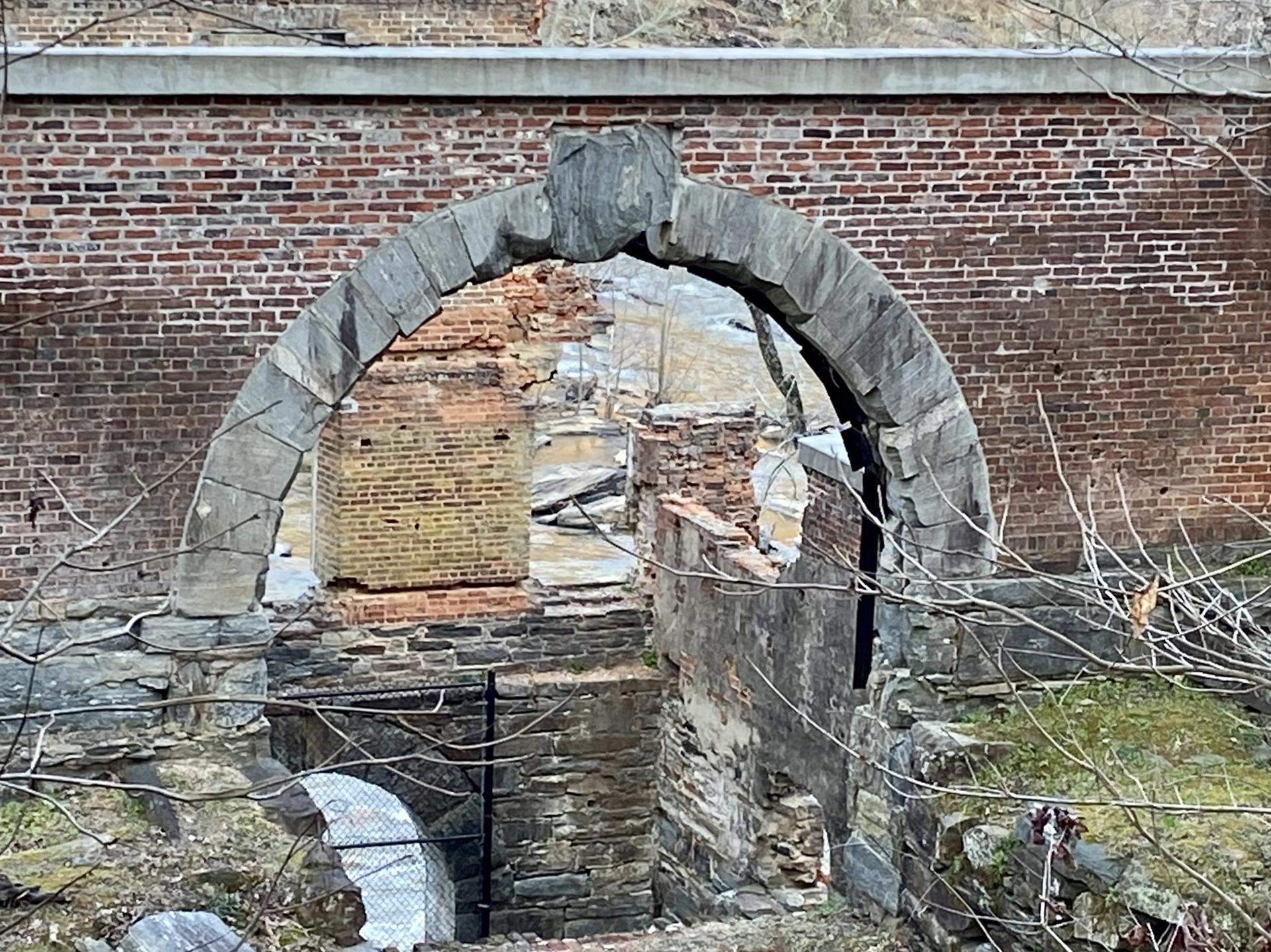 An old stone archway frames brick ruins against a larger brick wall.