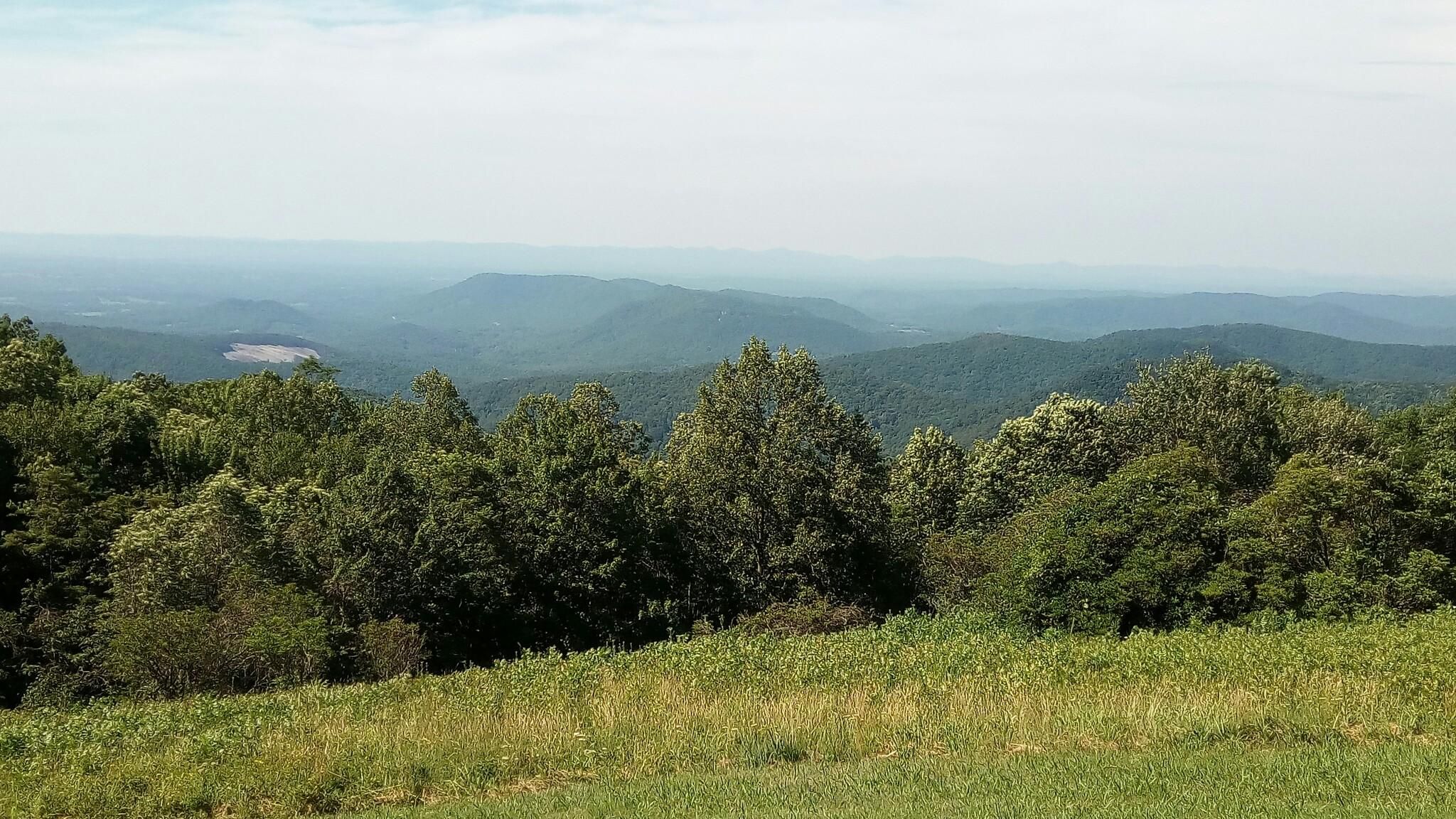 Vast mountain range vista with green trees and hazy distant peaks under bright skies. - Stone Mountain Overlook to Granite Quarry Overlook