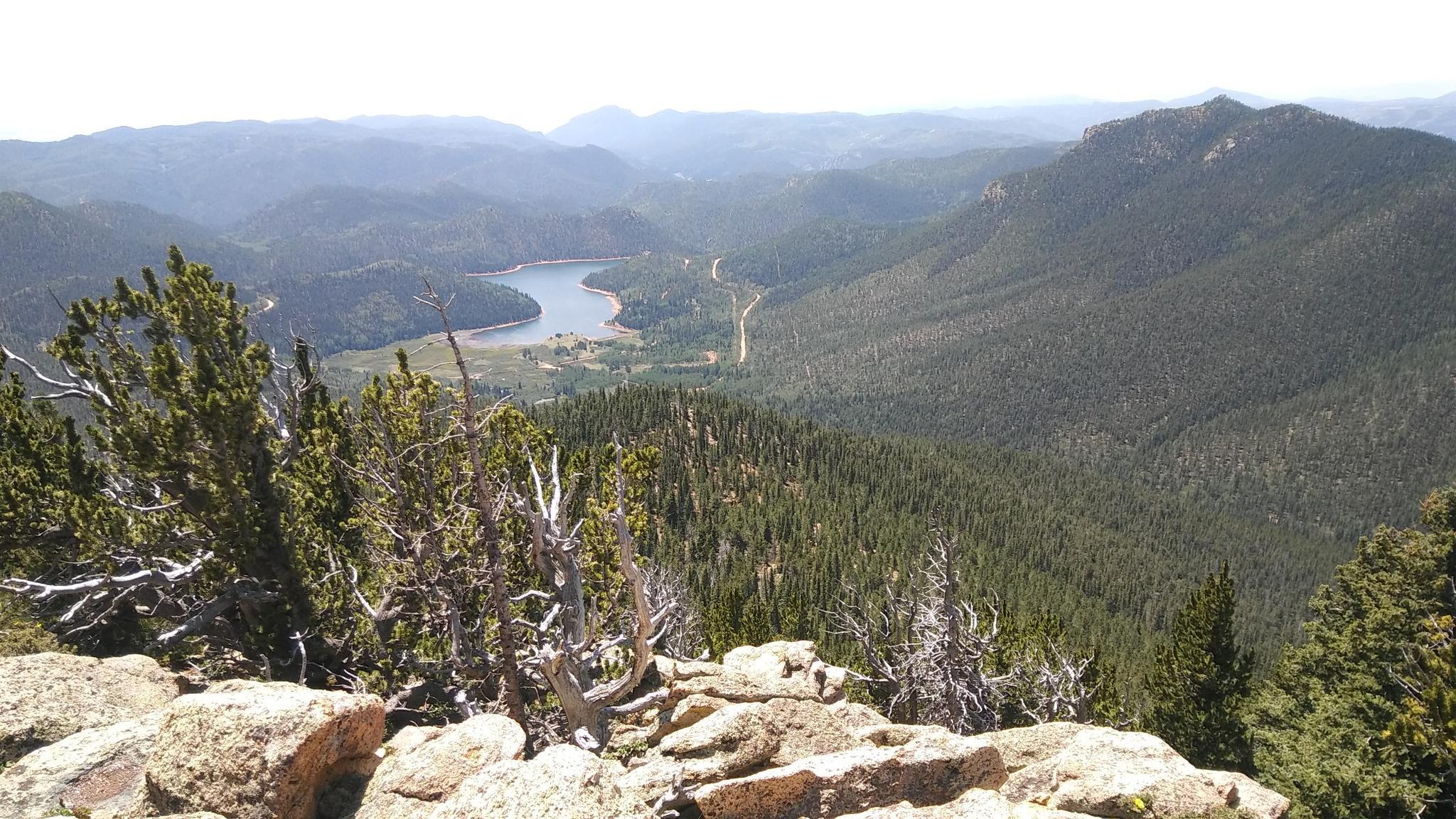 Panoramic view of a forested valley with a winding lake, from a rocky peak.