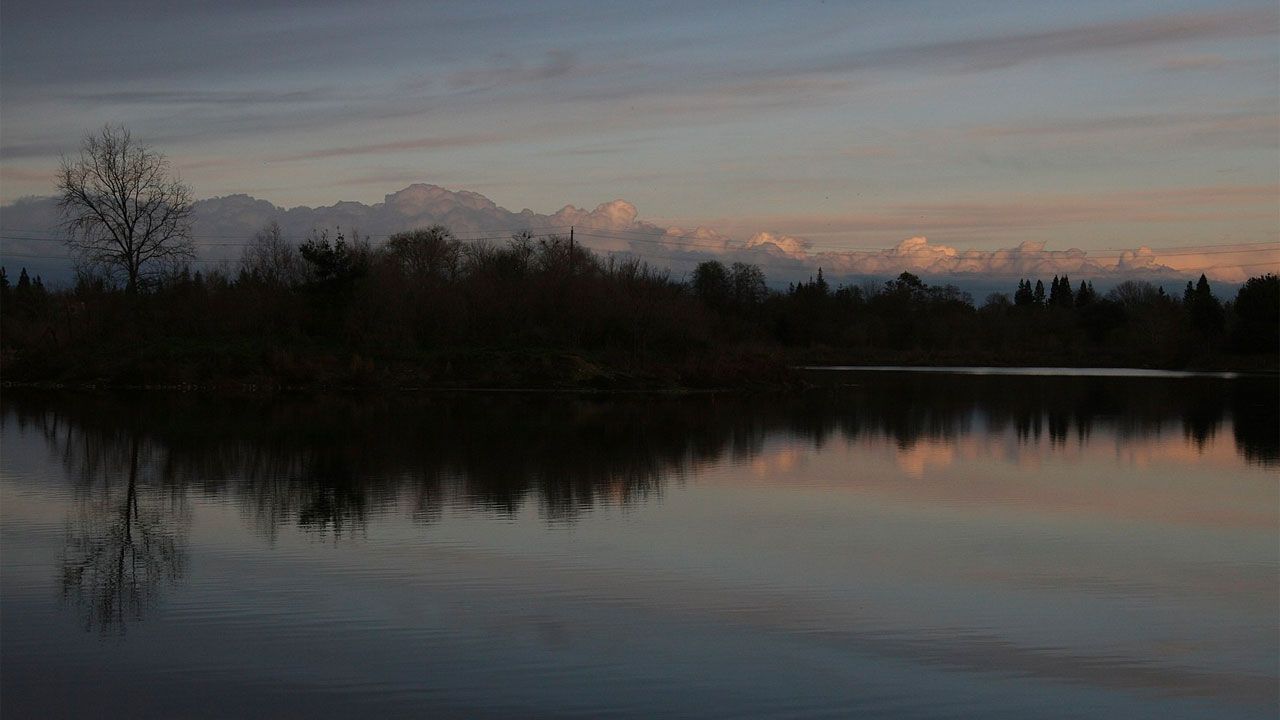 Calm lake reflecting dark trees and distant mountains under a twilight sky. - Sacramento River Bike Trail – Sacramento River loop from John F Kennedy High School