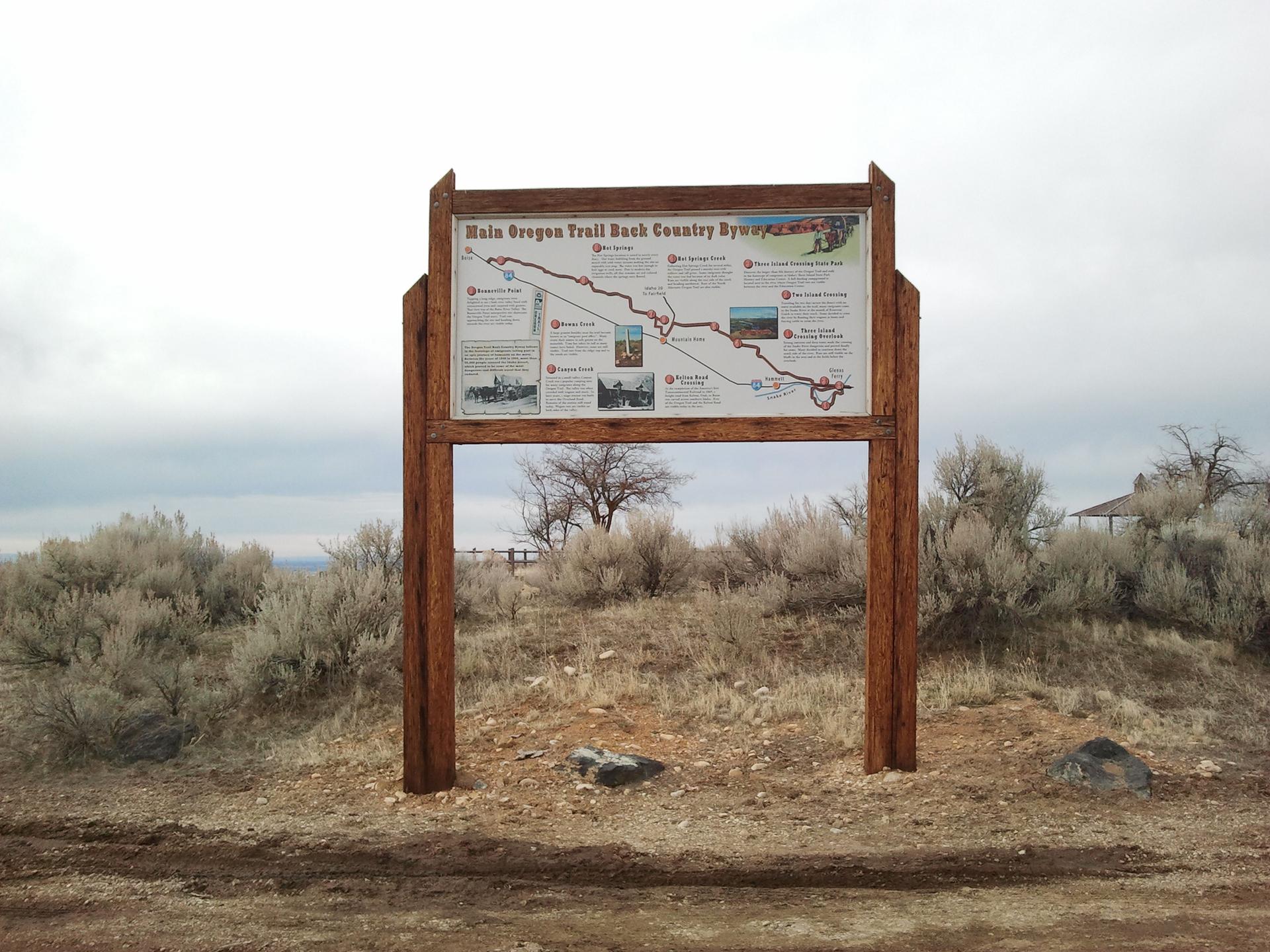 Large wooden information sign in a dry, brushy landscape under an overcast sky.