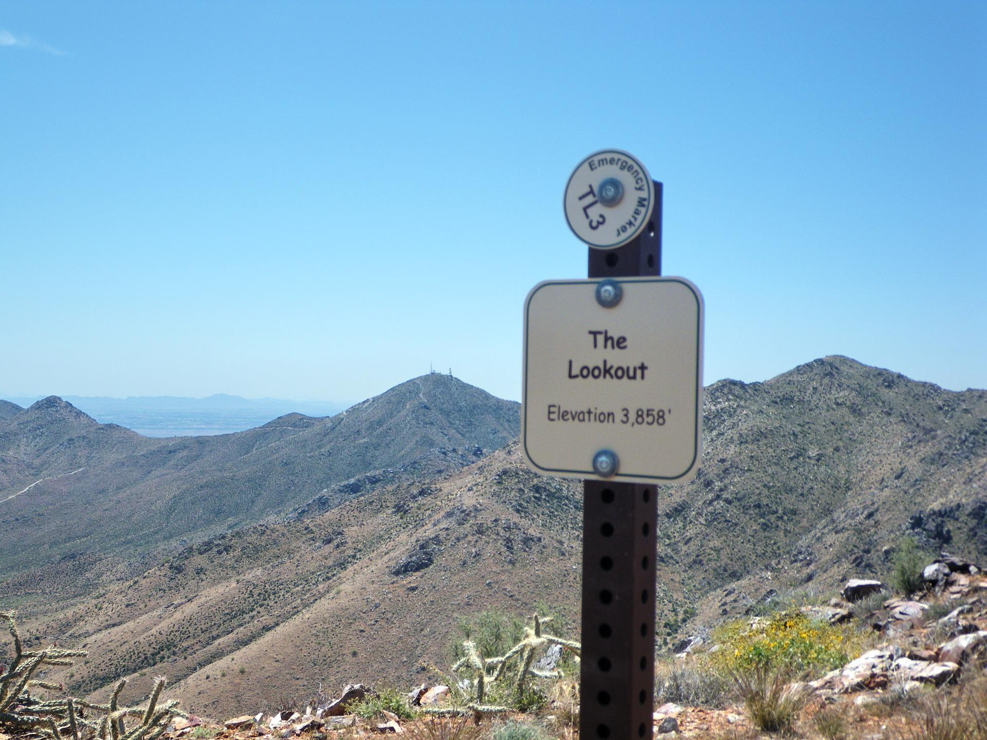 A lookout sign on a post overlooks arid mountains under a clear blue sky.