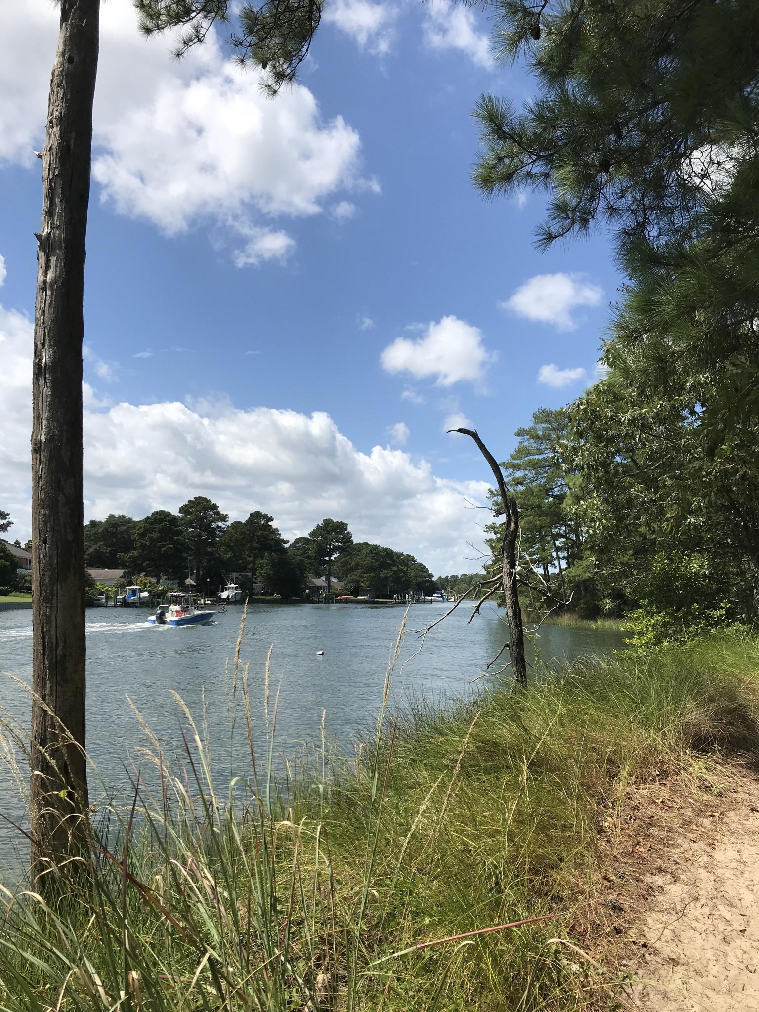A small boat cruises on a sunny waterway lined with trees.