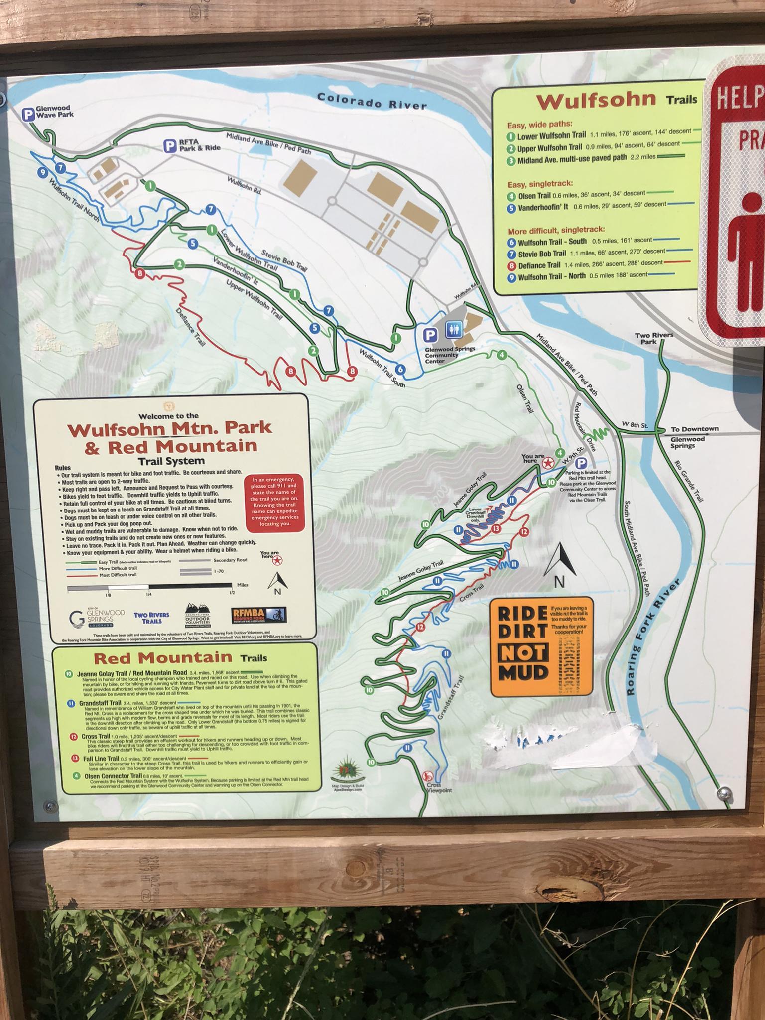 A detailed trail map displayed on a wooden sign outdoors.
