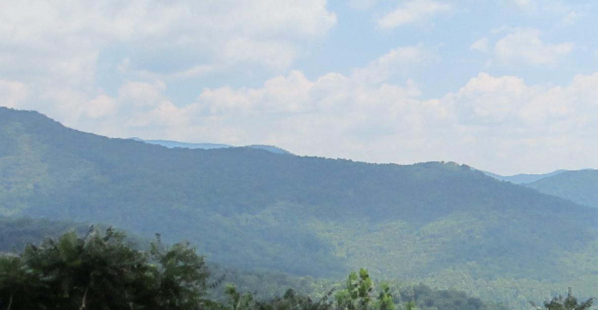 Layers of green forested mountains under a bright, cloudy sky.