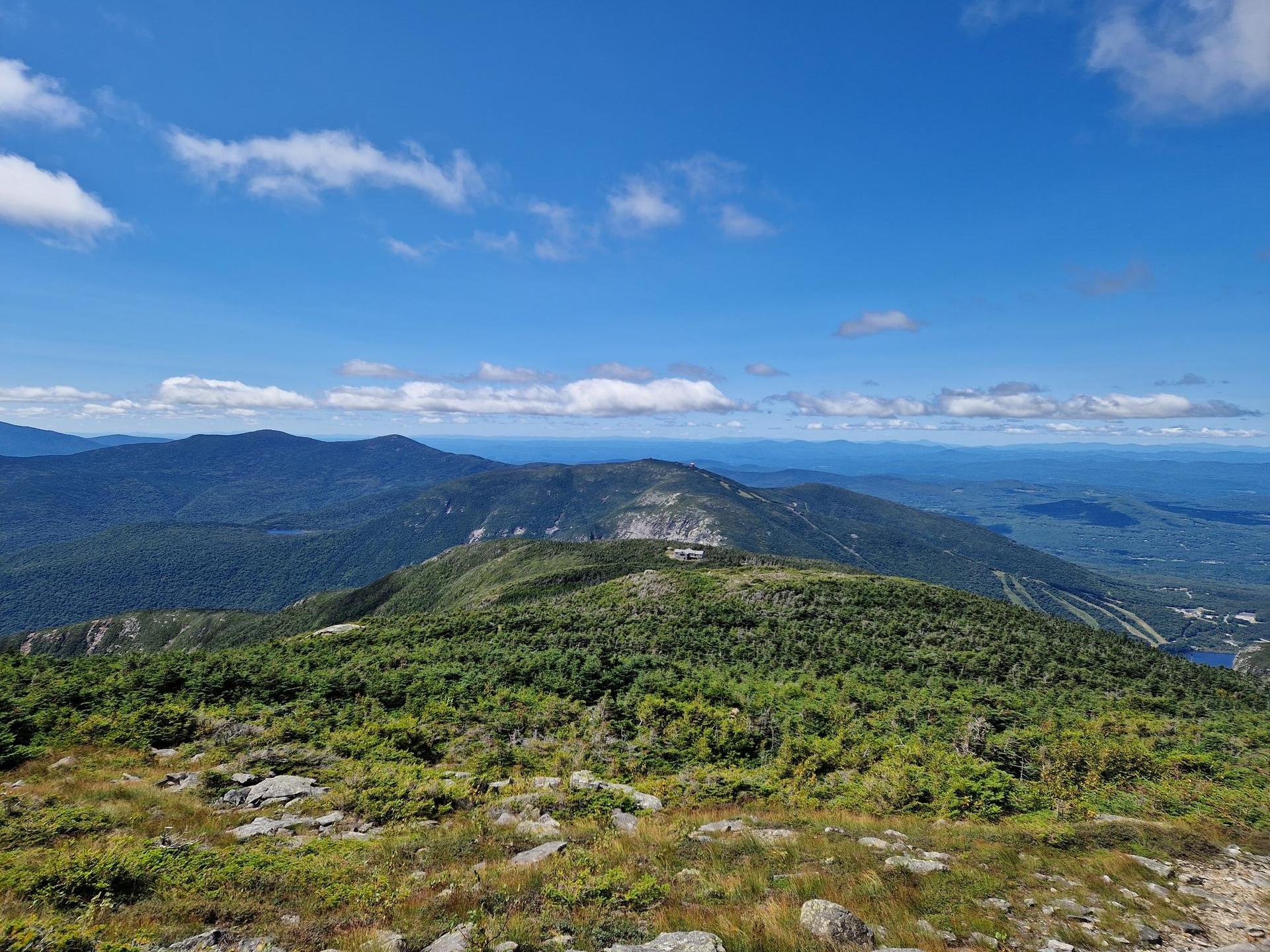 Panoramic view of green mountain ranges under a bright blue sky with clouds.
