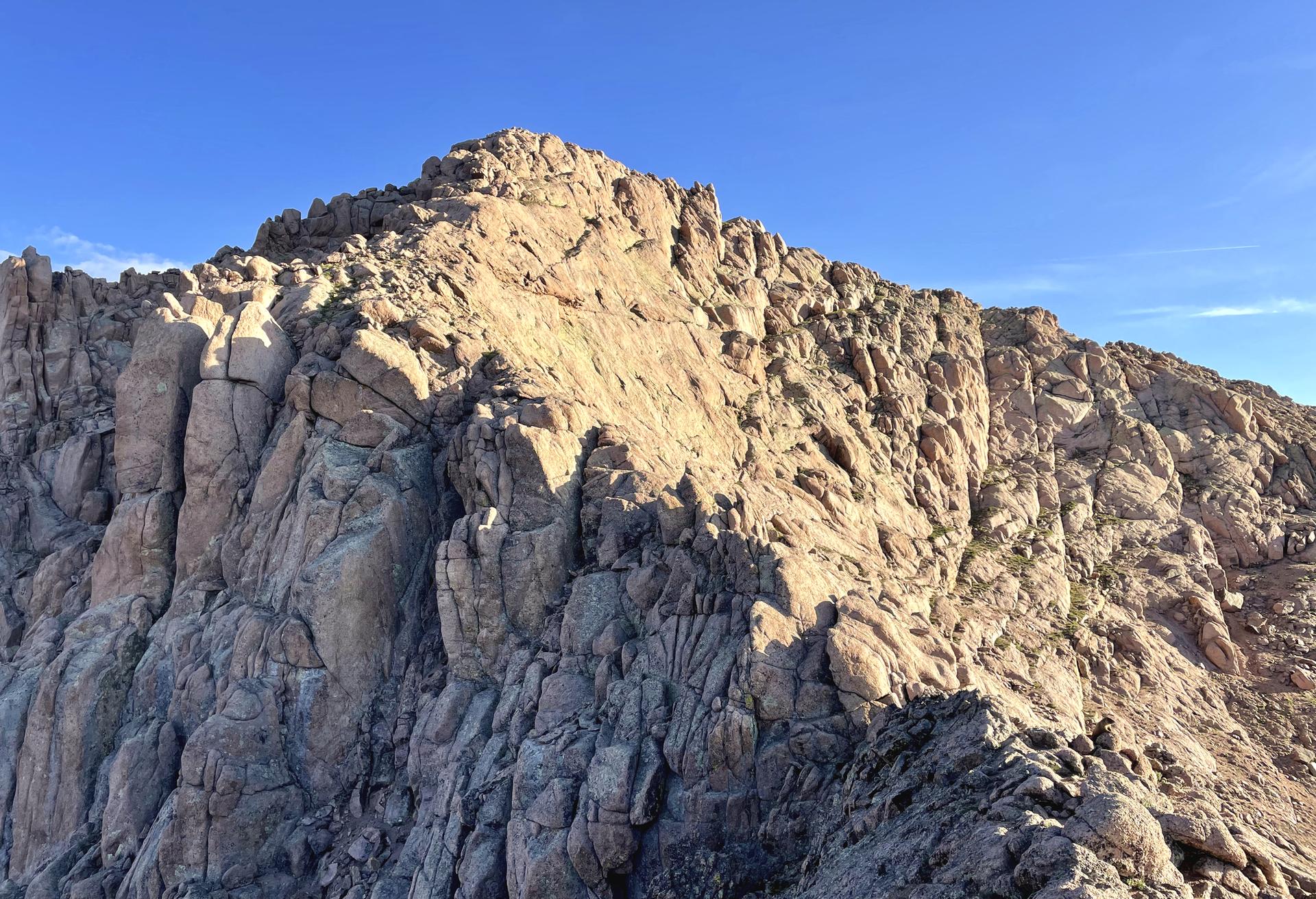 A rugged, sunlit rocky mountain peak under a clear blue sky.