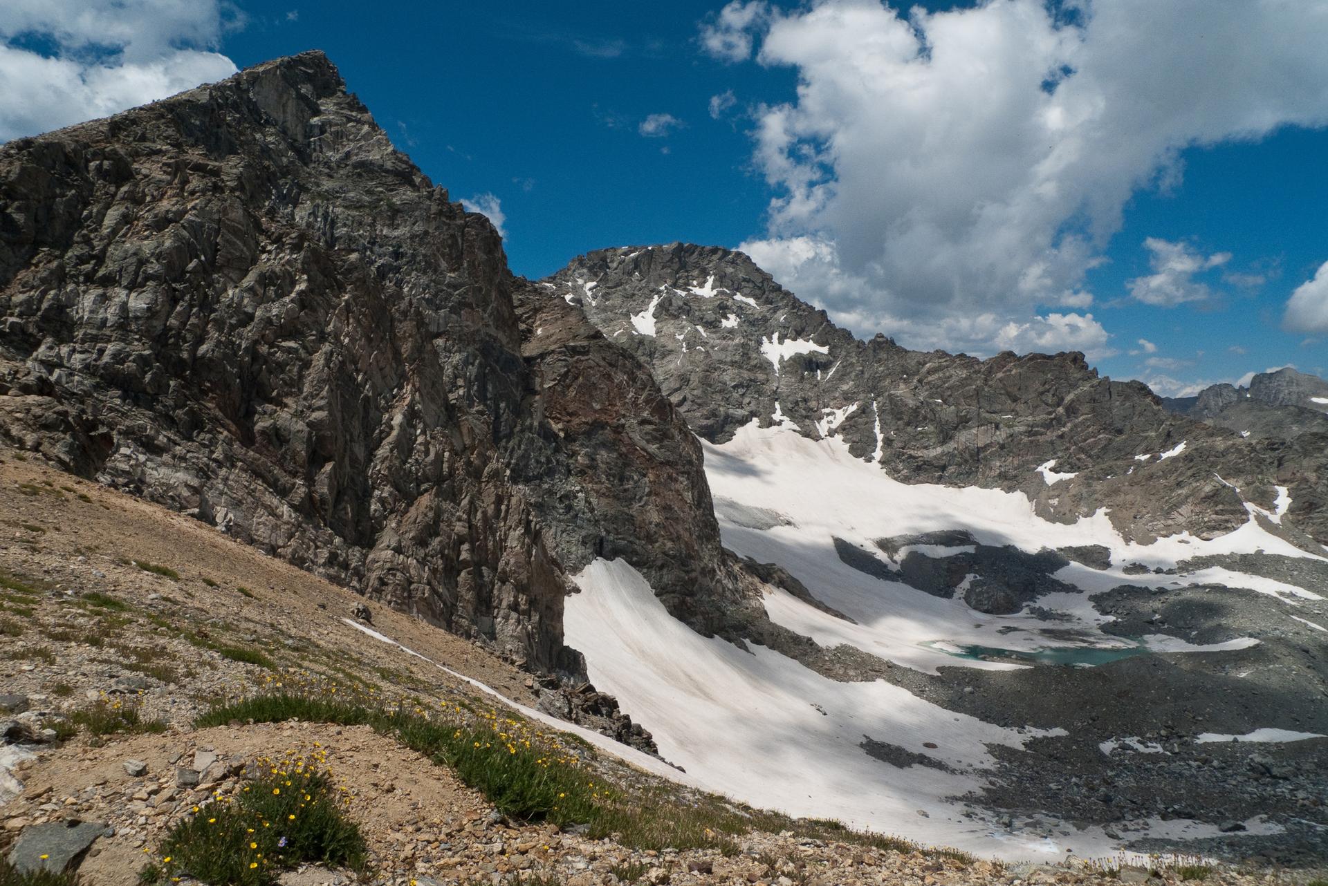 Rugged mountains with snow patches under a bright, partly cloudy sky.