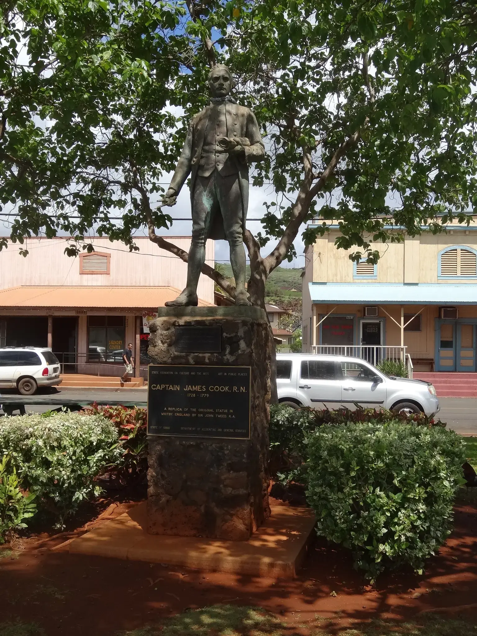 Bronze statue of a man in historical attire under trees in a town.