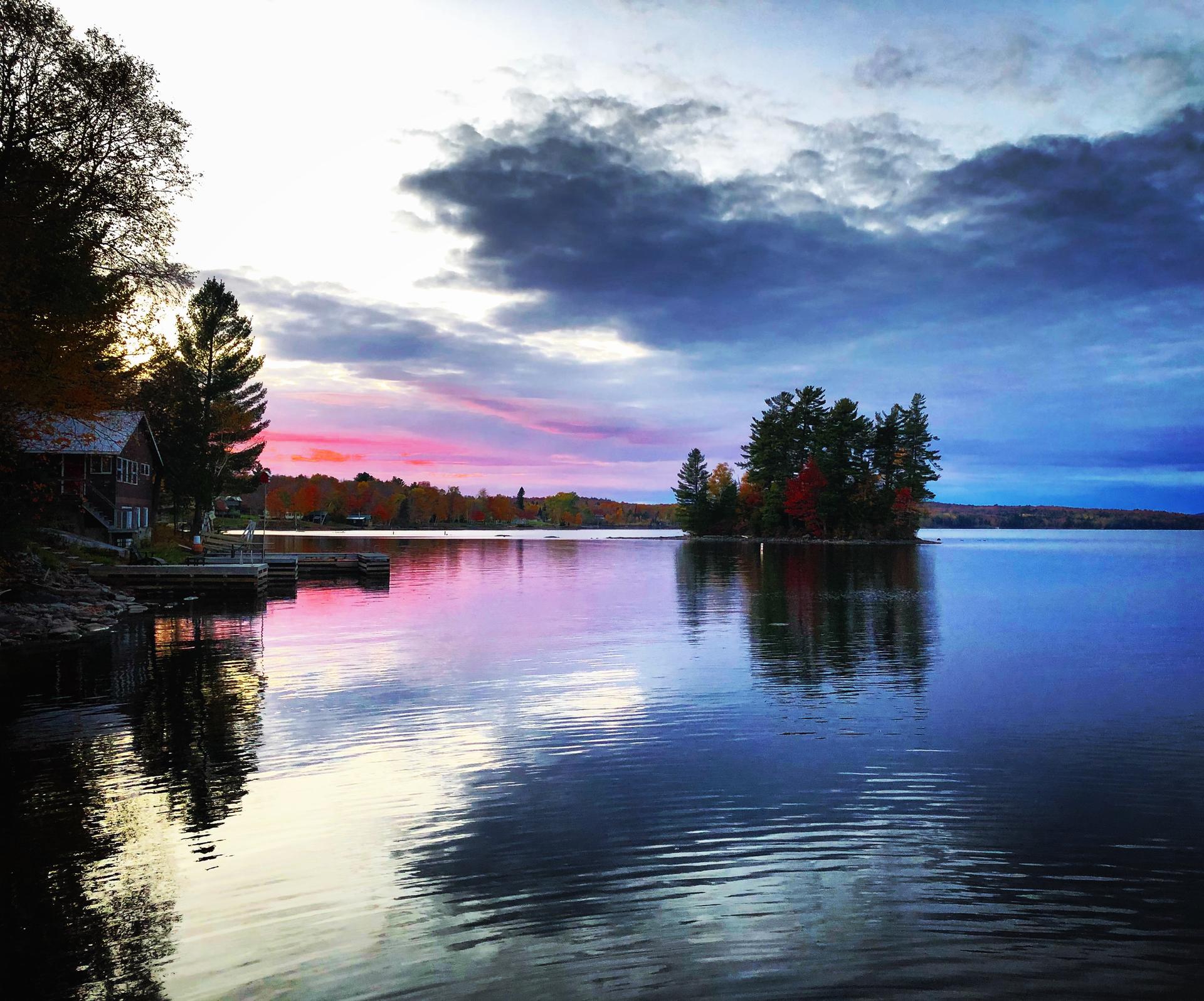 Vibrant sunset over a calm lake with a small tree-covered island.