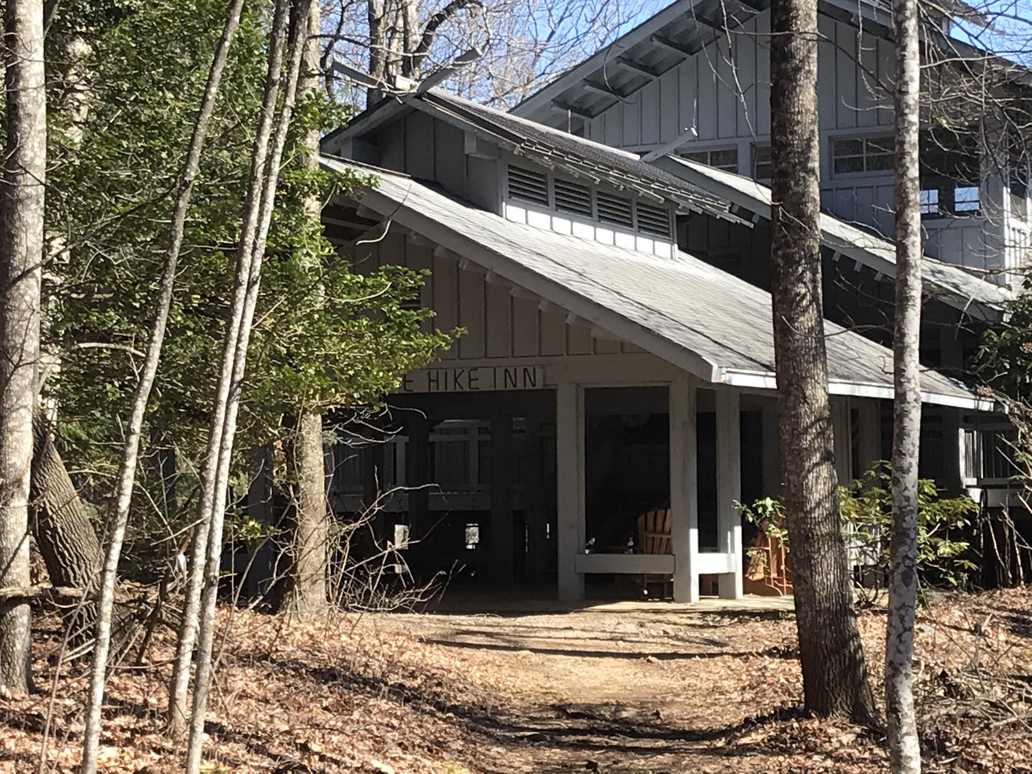 A rustic wooden building entrance with a covered porch, surrounded by trees.