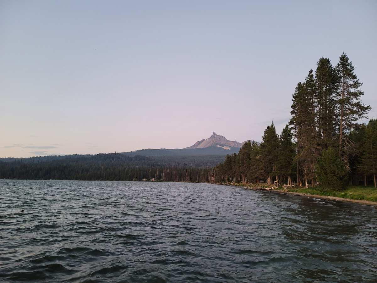 Dark lake with a forested shoreline and a distant peak under an evening sky.