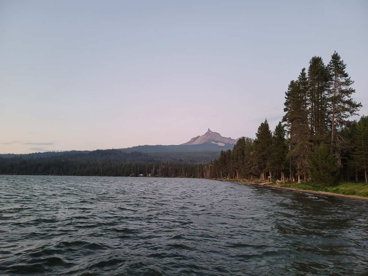 Dark lake with a forested shoreline and a distant peak under an evening sky. - Diamond Lake Loop