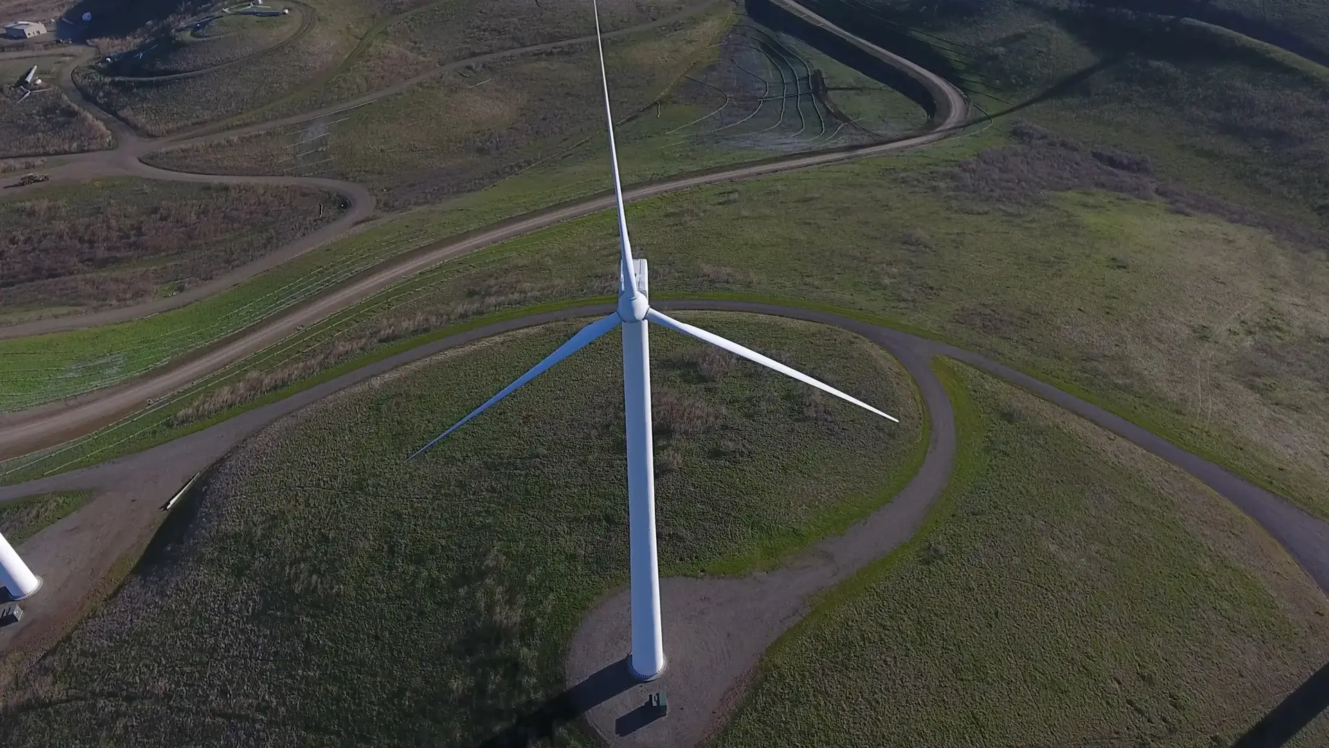 An aerial view of a large white wind turbine on green rolling hills.