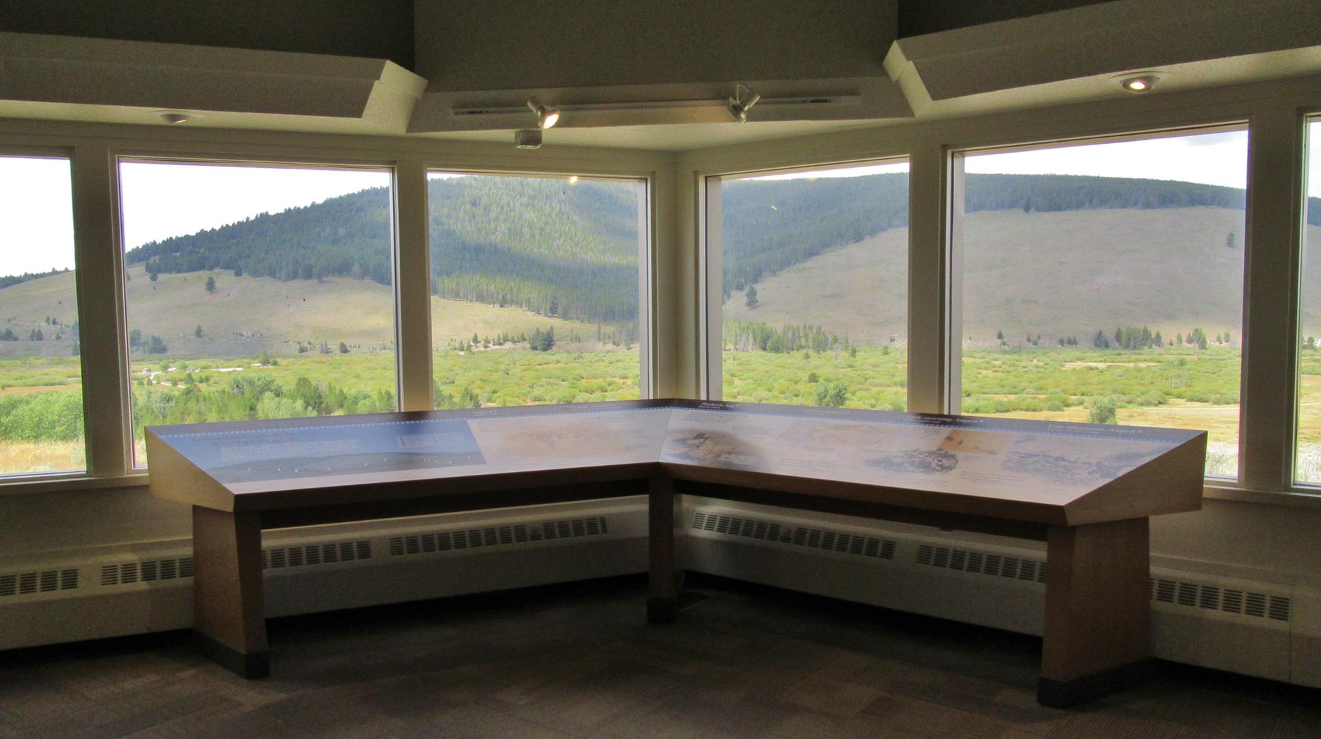 An indoor viewing room with large windows overlooks green hills and valleys.