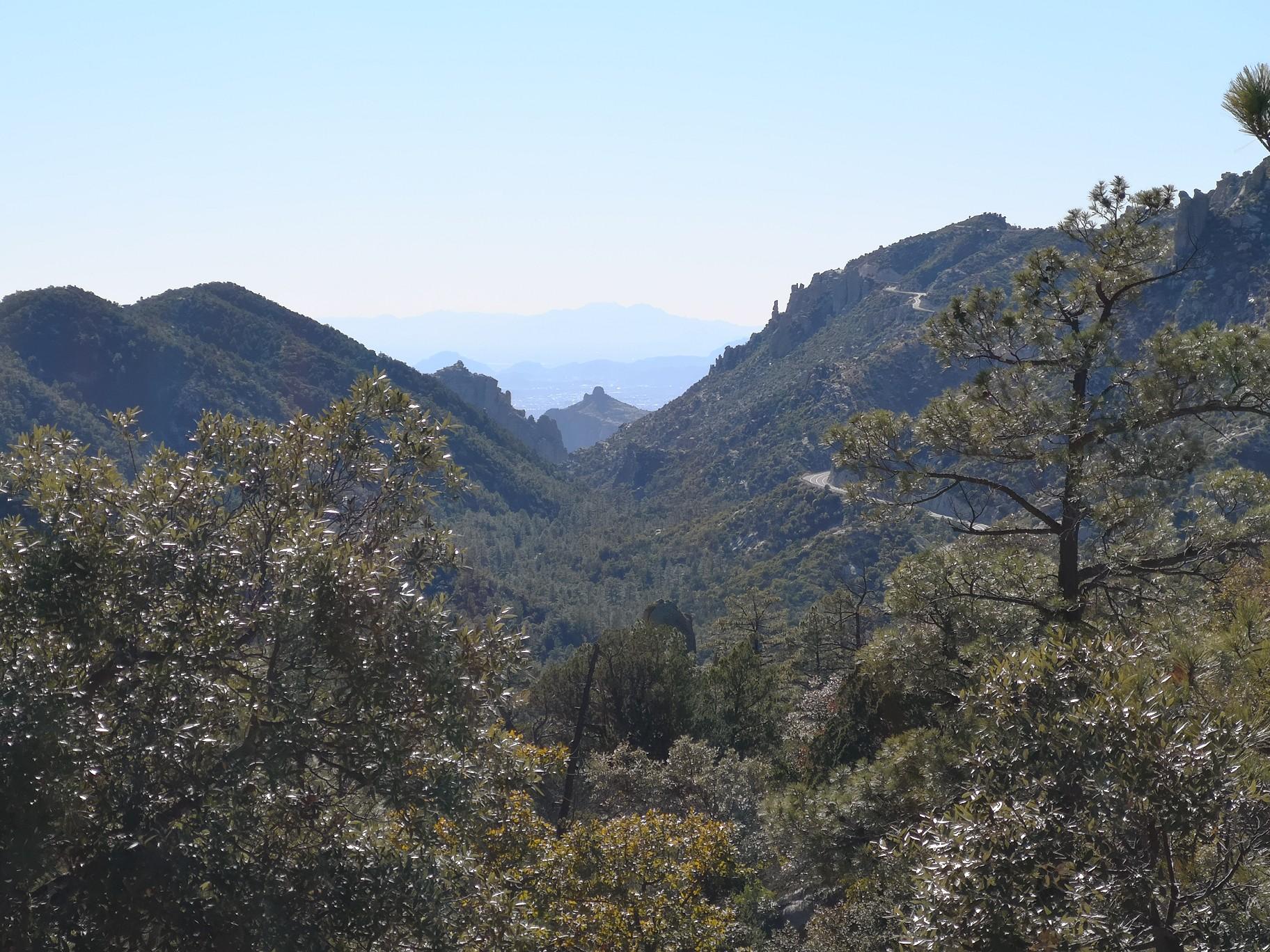 Lush green mountain valley with distant hazy peaks under bright sky.