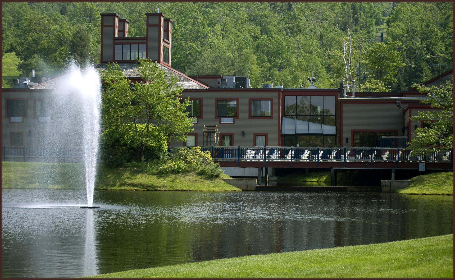A large building with a fountain in a lake, surrounded by green trees.