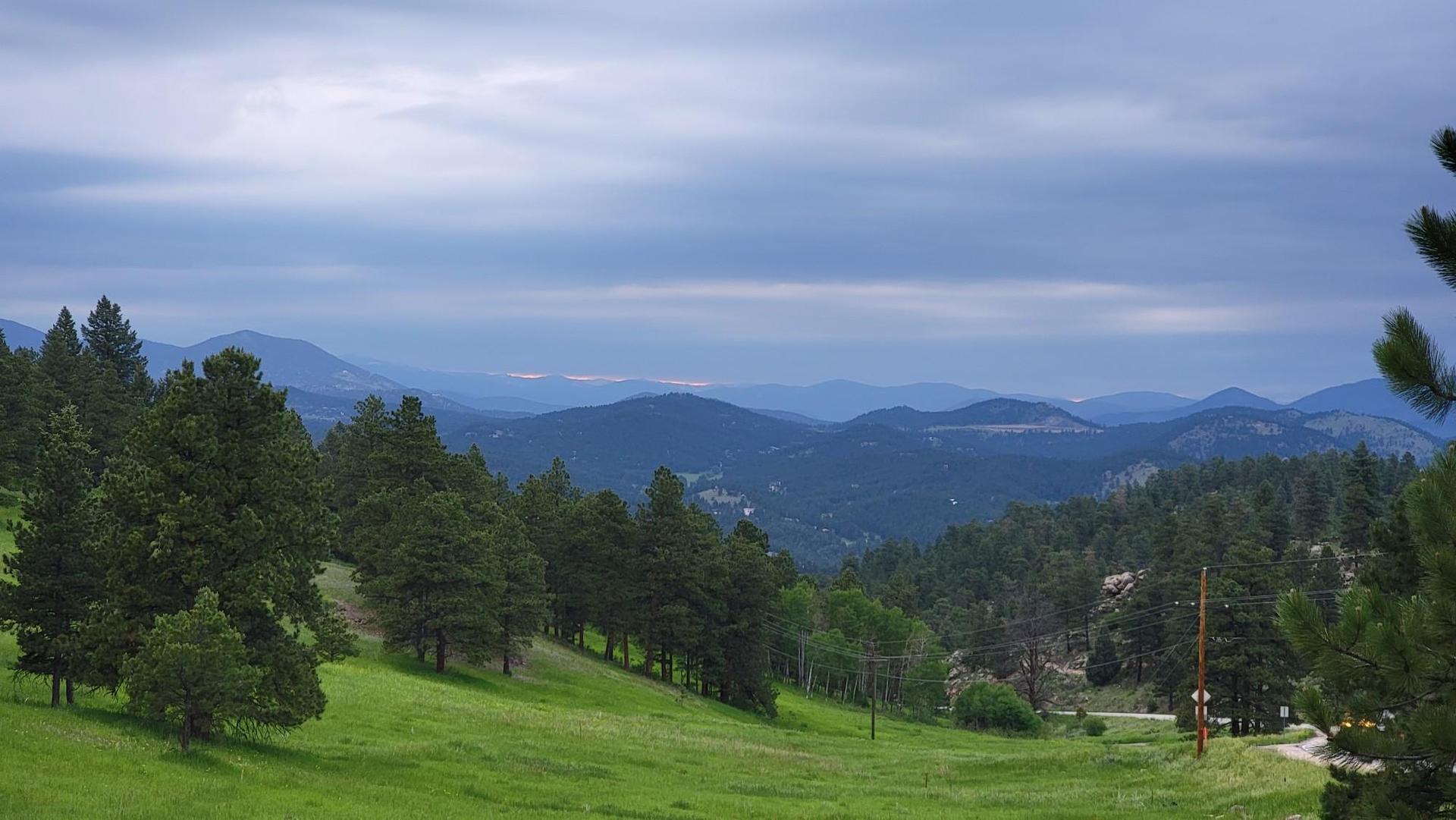 Panoramic view of green hills and distant mountains under a cloudy sky.