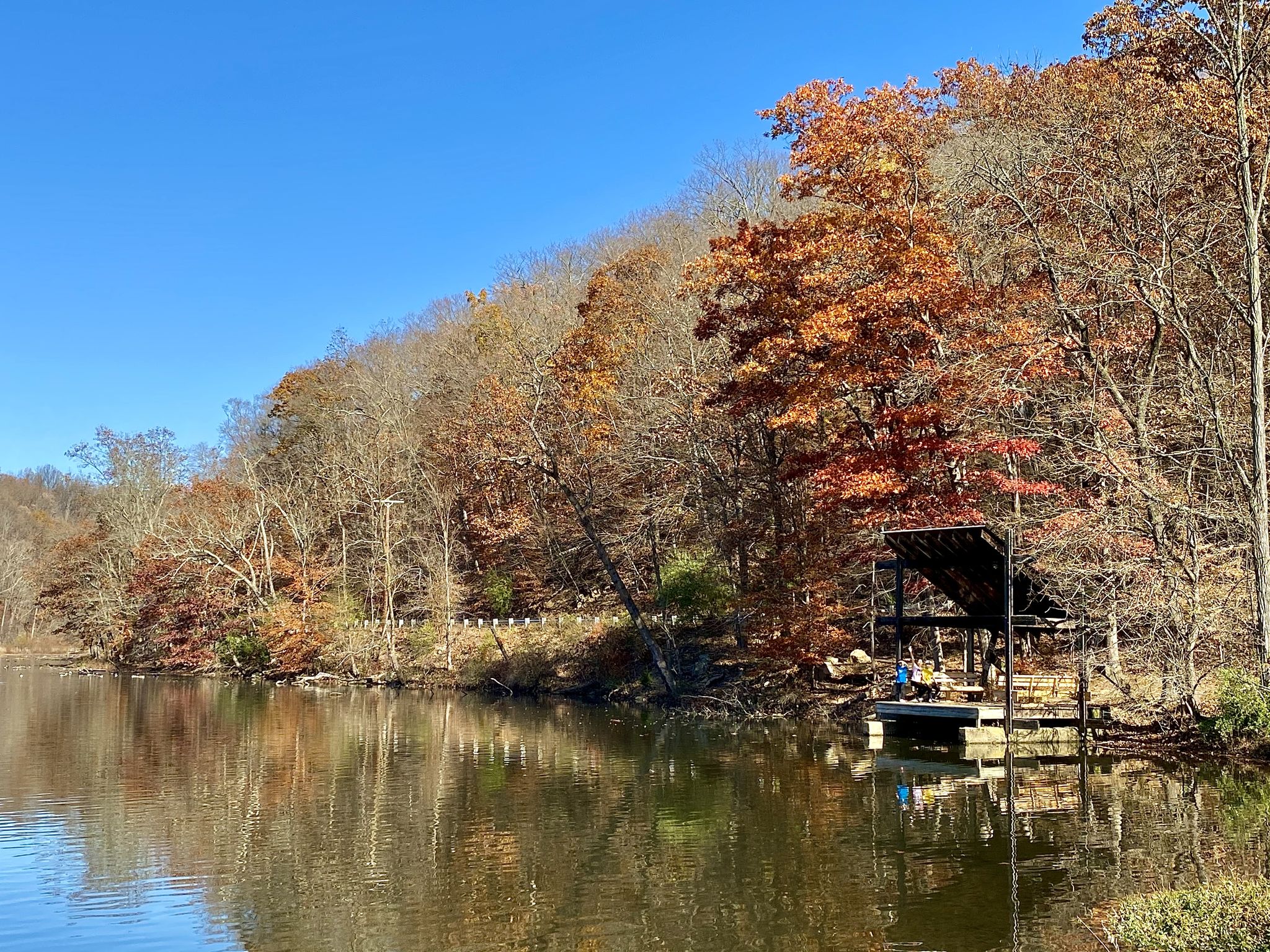 A calm lake reflects autumn trees and a boathouse on a sunny day. - Lake Solitude and Waterfall – Railroad Ruins loop from High Bridge