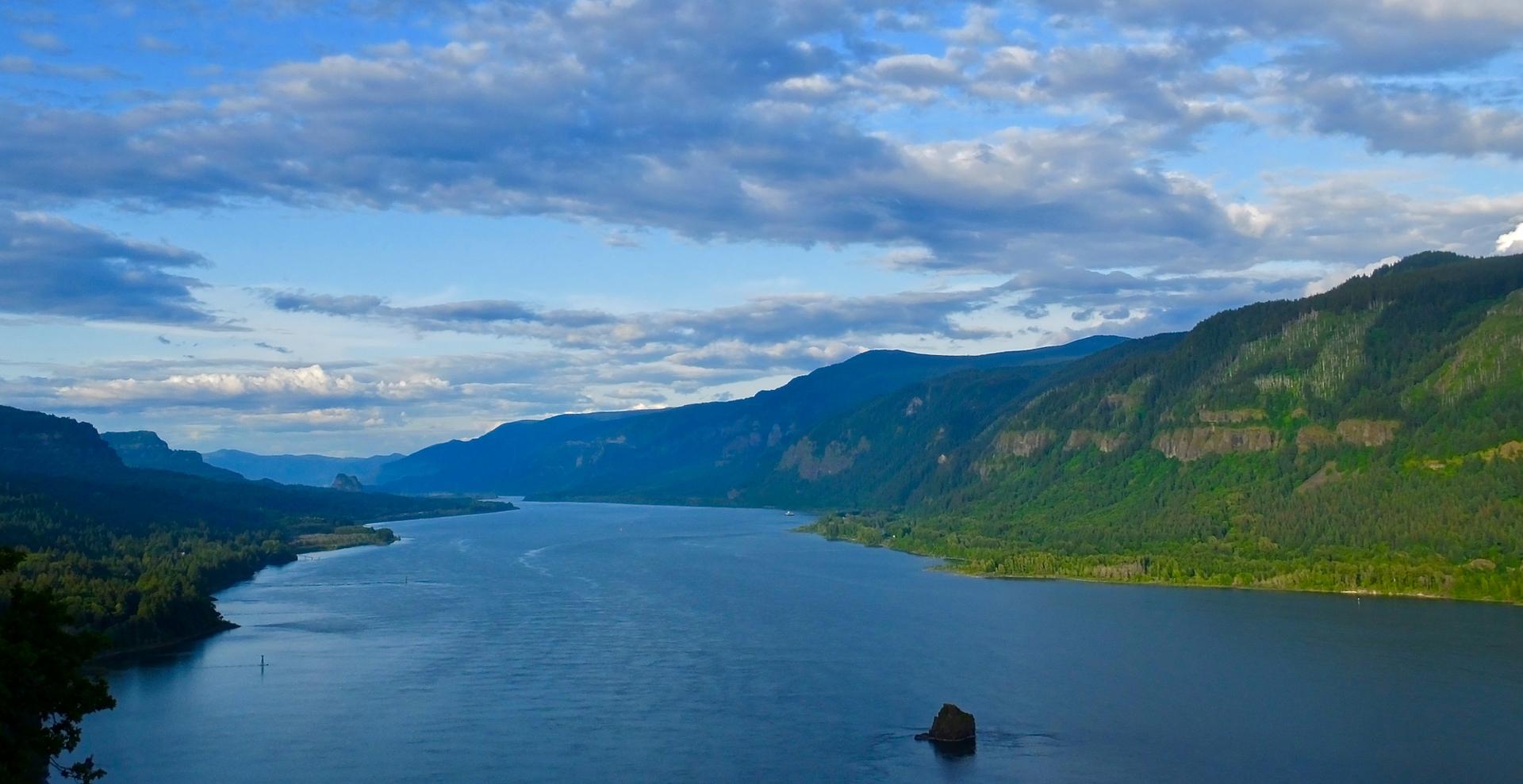 Panoramic view of a wide river winding through forested mountains.