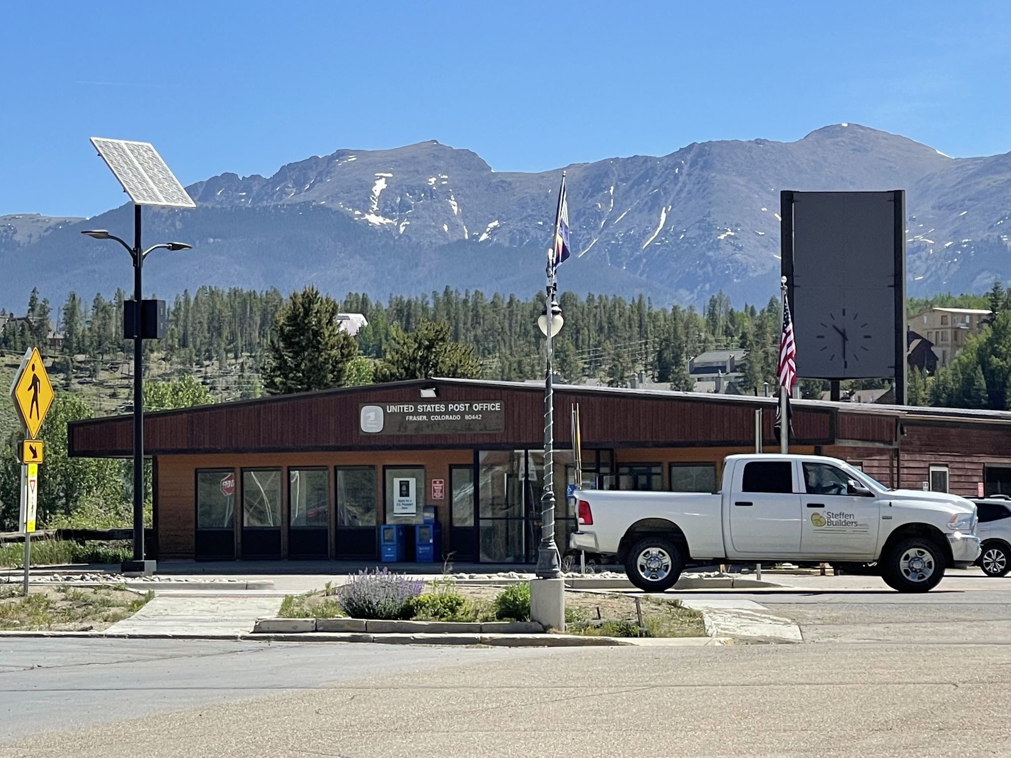A post office building with a white truck and distant snowy mountains. - Fraser – Colorado River loop from Fraser-Winter Park