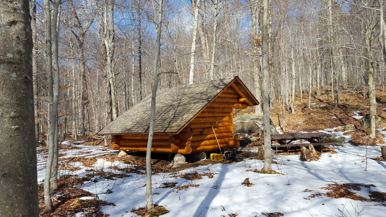 Rustic log cabin nestled in a snowy forest with bare trees. - Bear Lake Trail