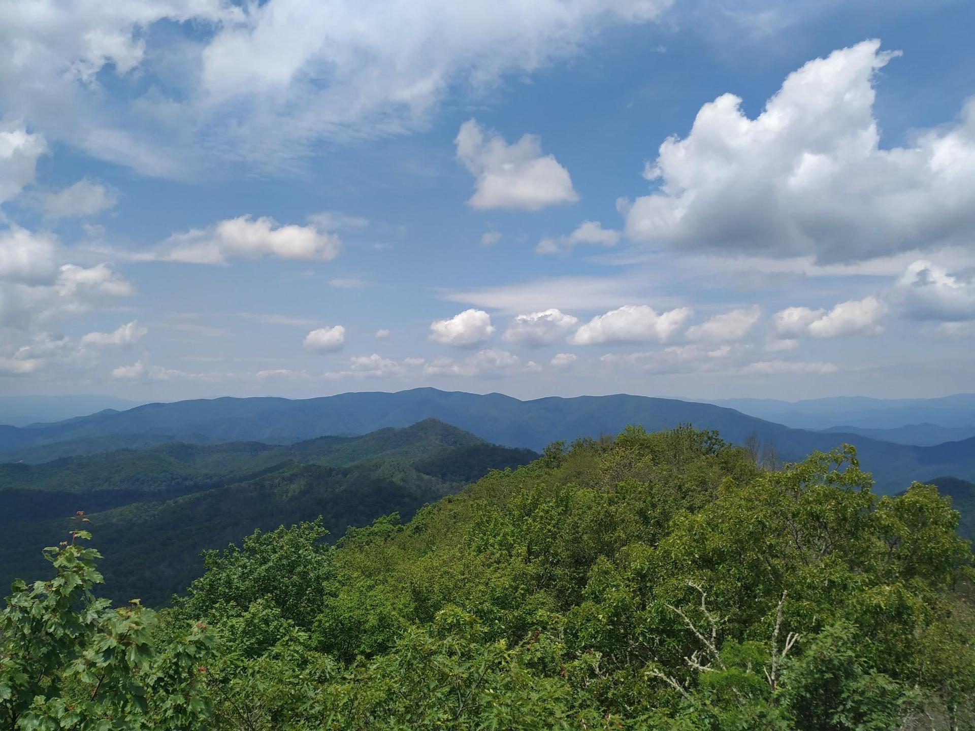 Expansive view of lush green mountains under a bright blue sky with clouds.