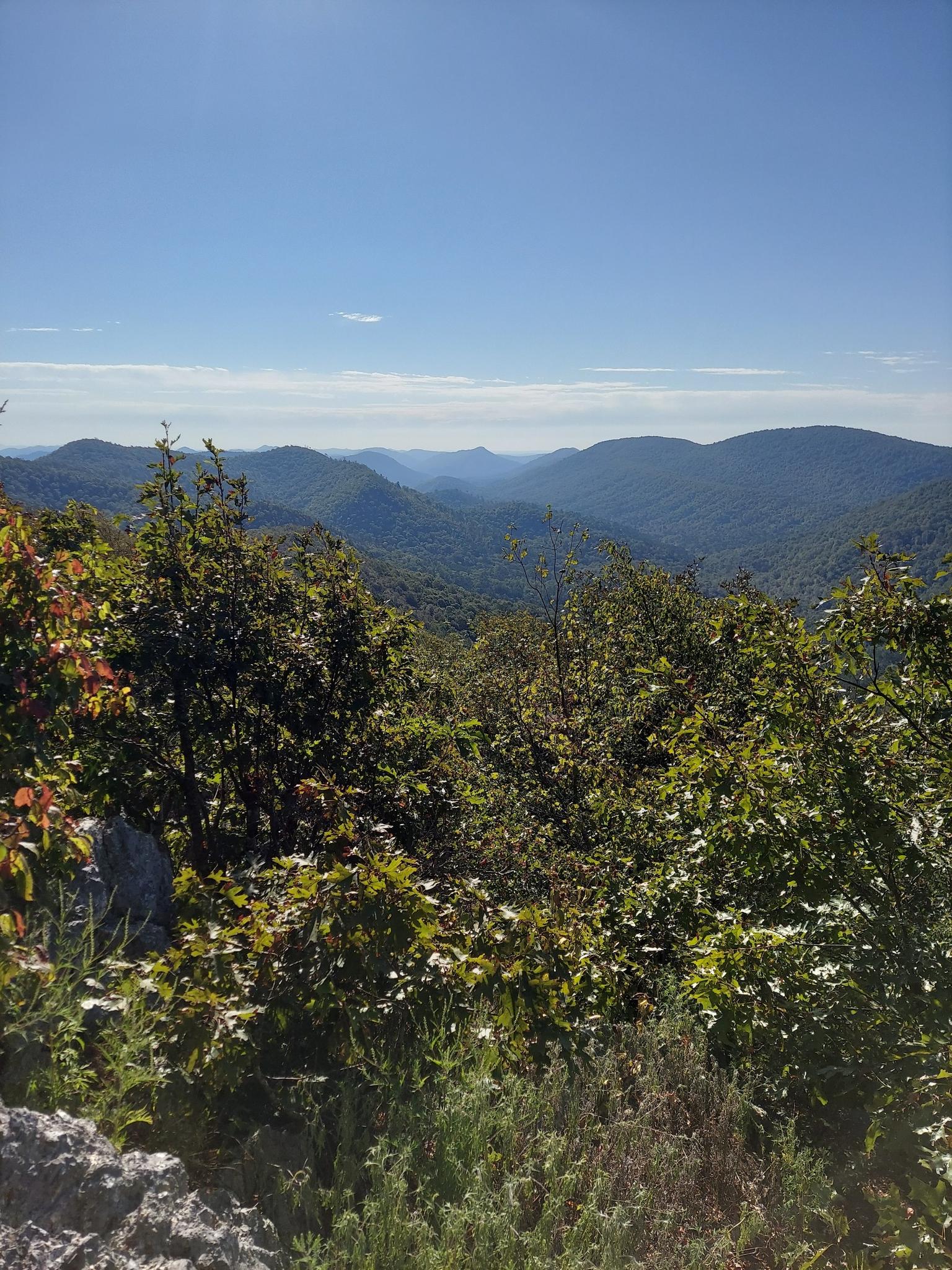 Sunny mountain vista with layers of green hills and a clear blue sky.